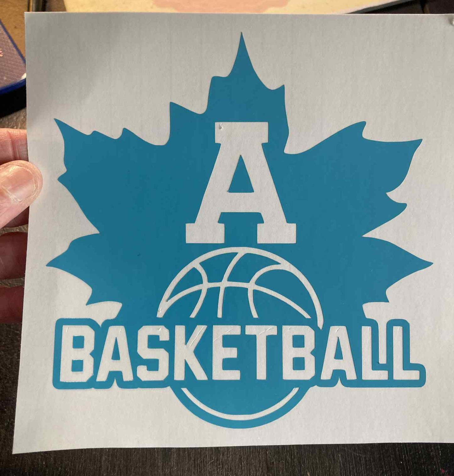 Blue basketball decal with a maple leaf design held by a hand on a dark surface.
