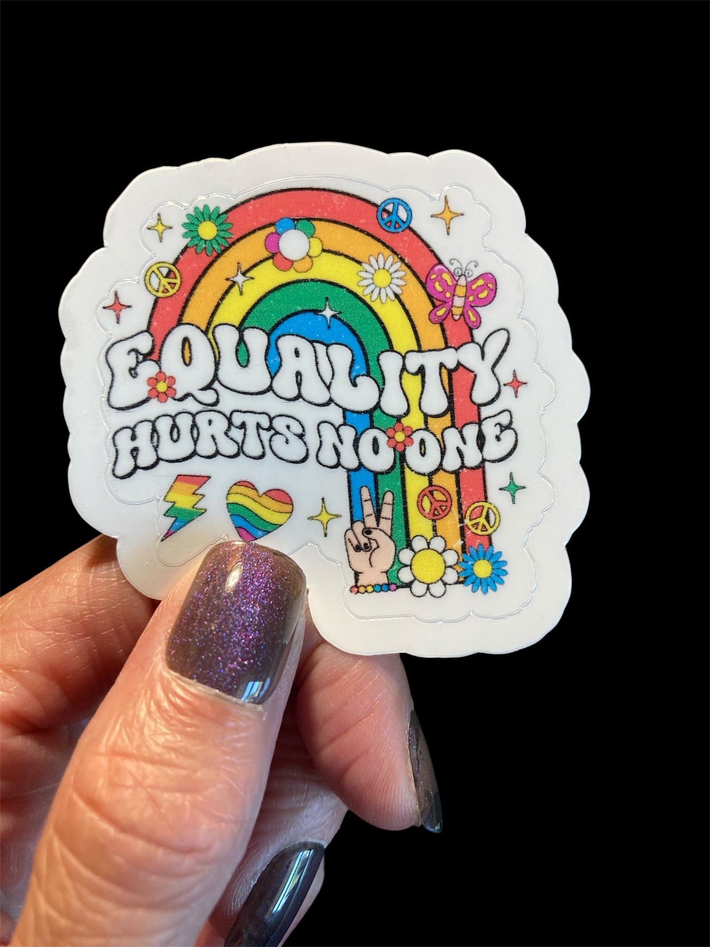 Sticker with rainbow design and text held by a hand against a black background