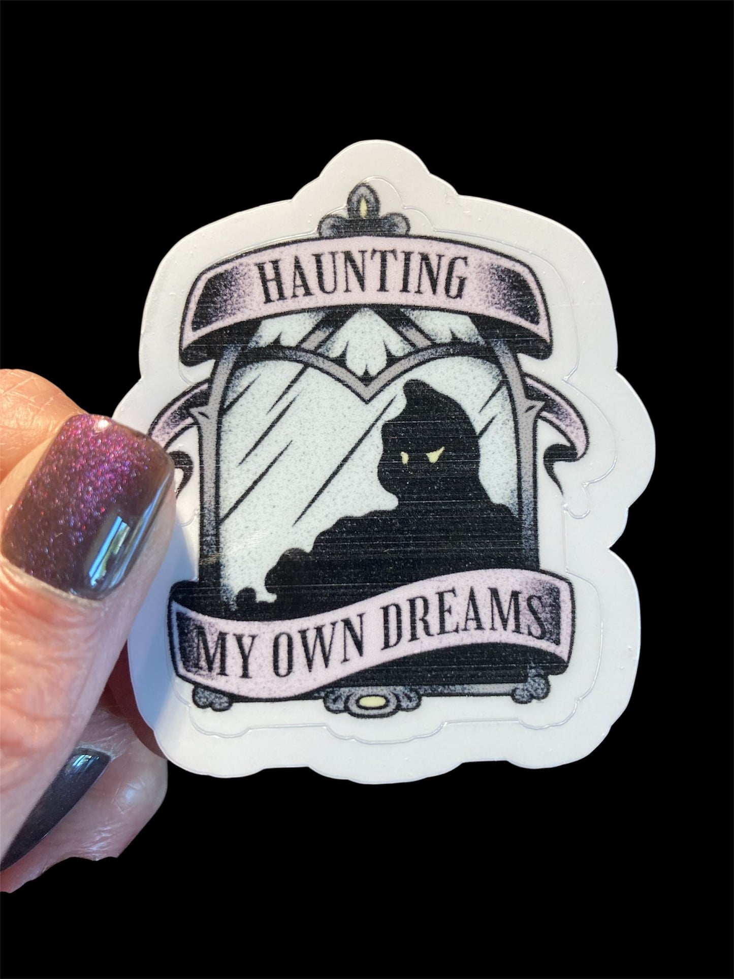 Sticker with a black cat silhouette and text 'Haunting My Own Dreams' held by a hand.