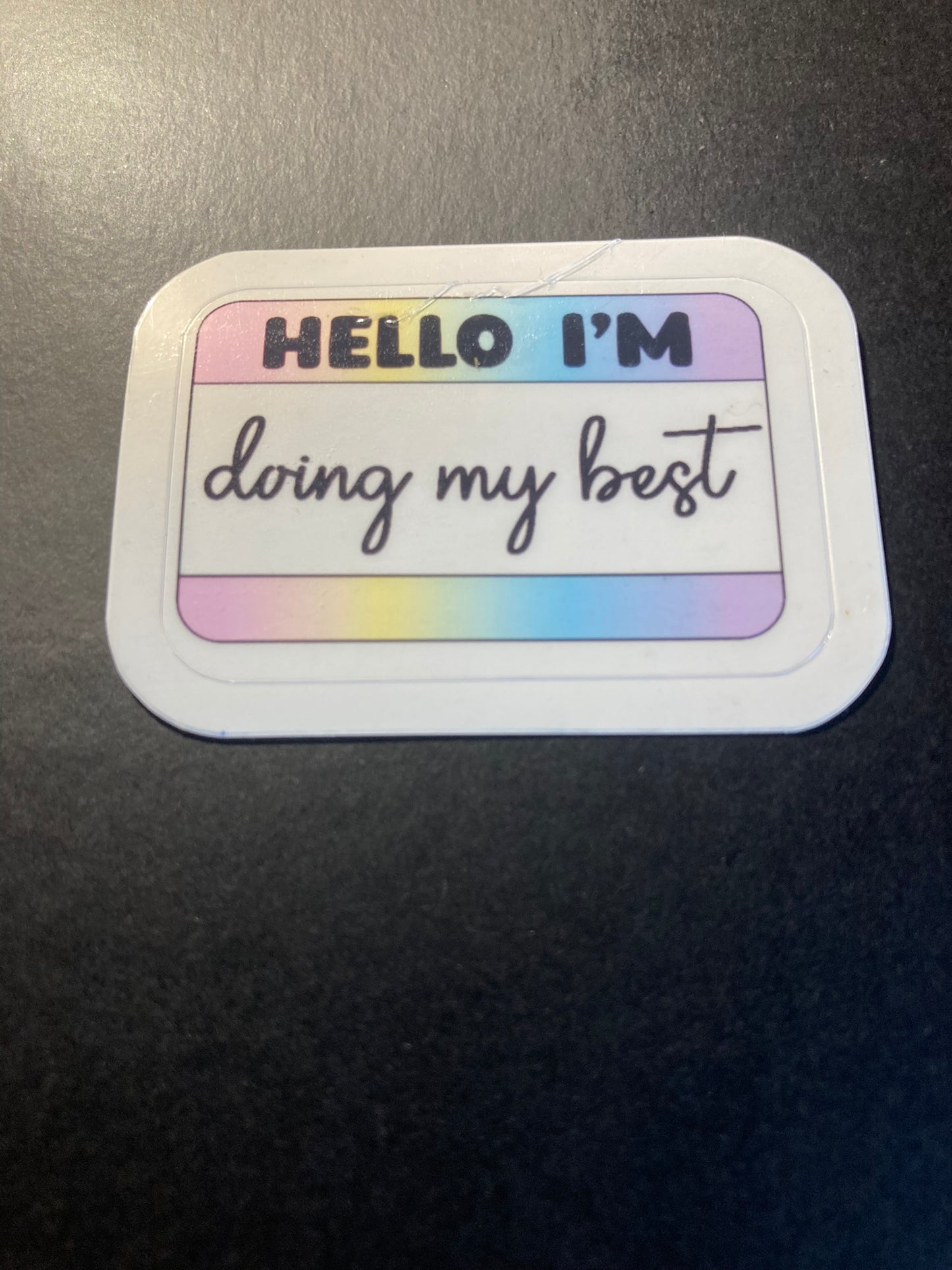 Sticker with 'Hello I'm doing my best' text on a gradient background, attached to a dark surface.