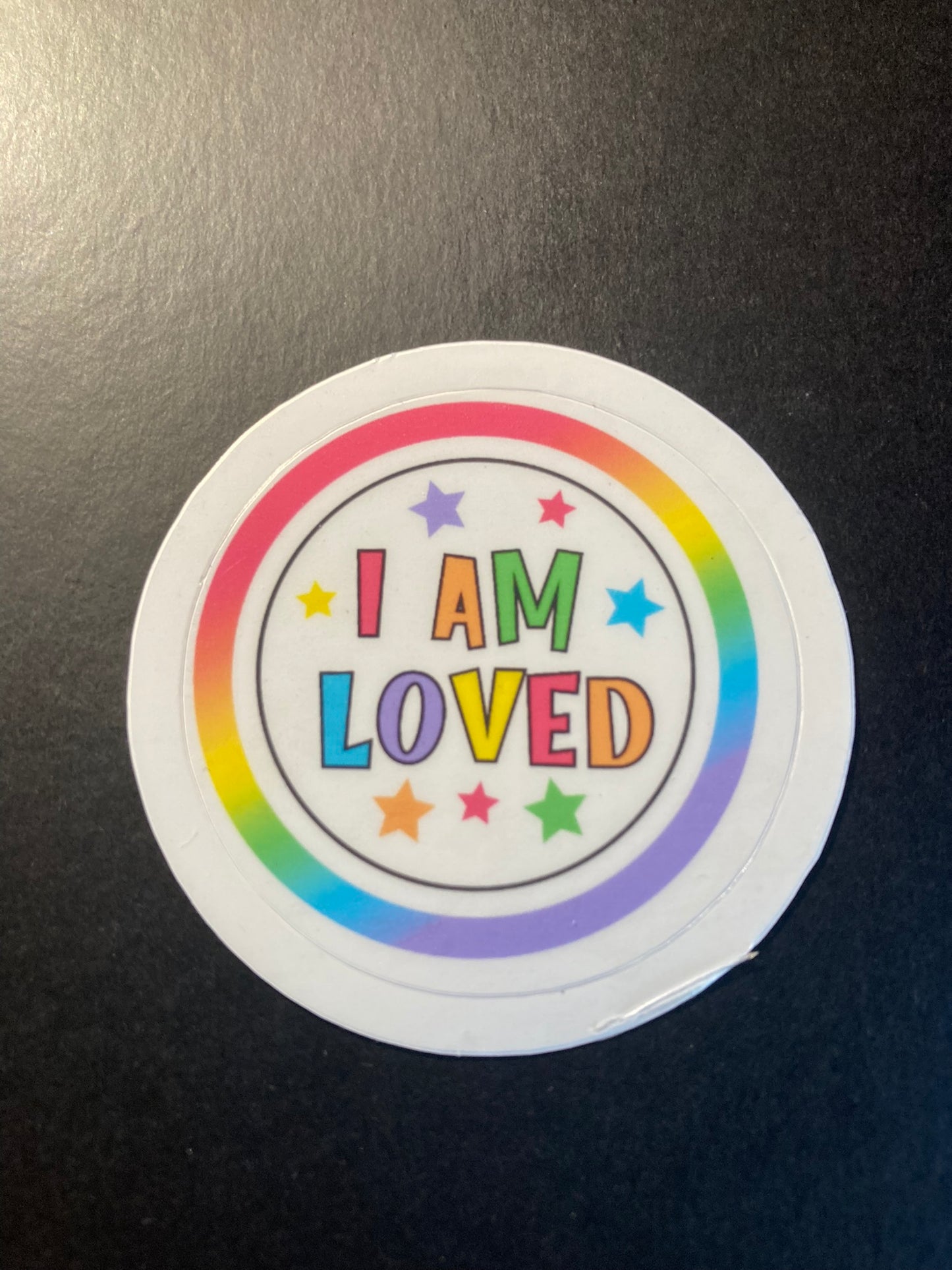 Round sticker with 'I AM LOVED' text on a black background