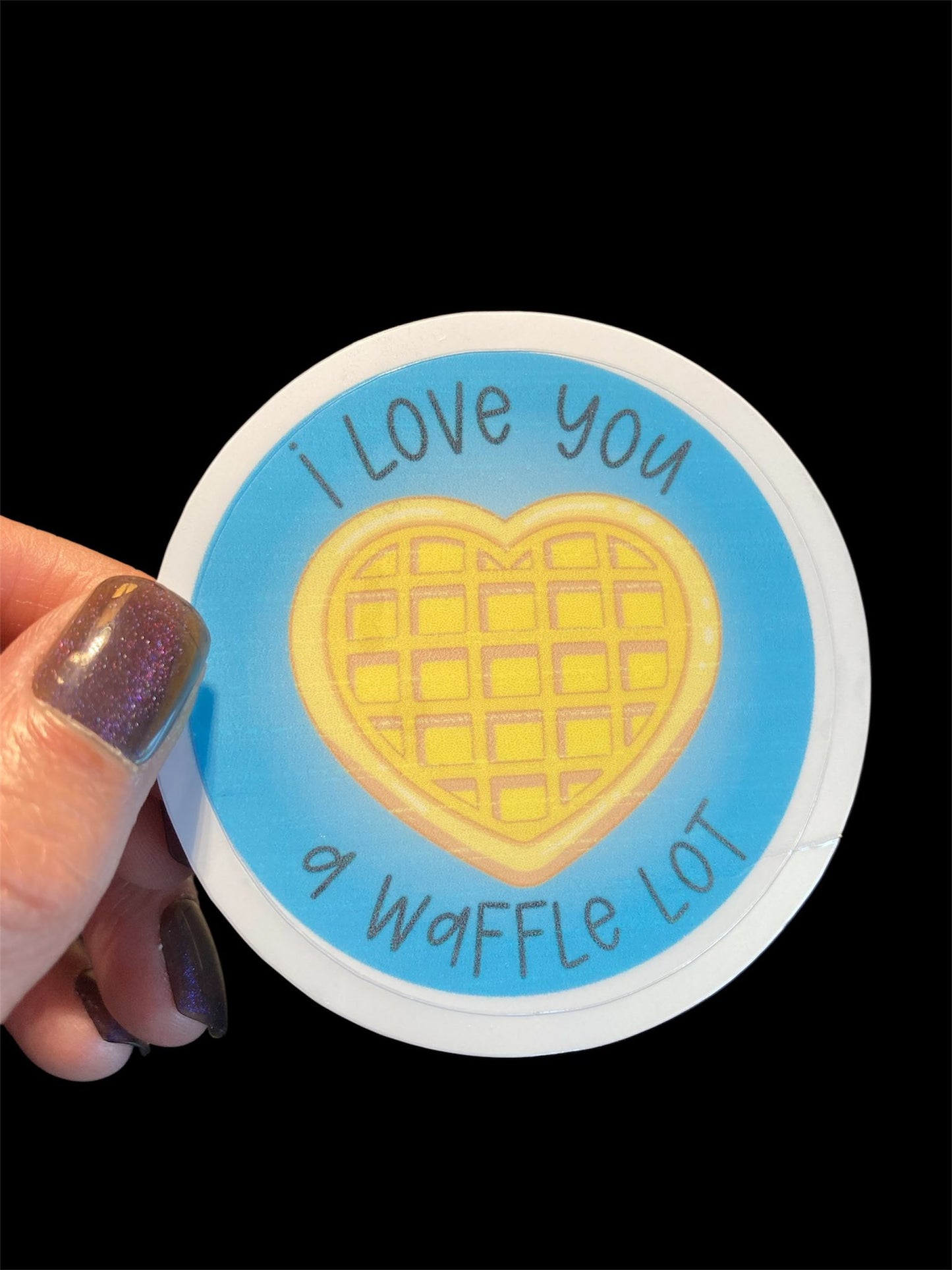 Sticker with a heart-shaped waffle and text 'I love you a waffle lot' held by a hand.