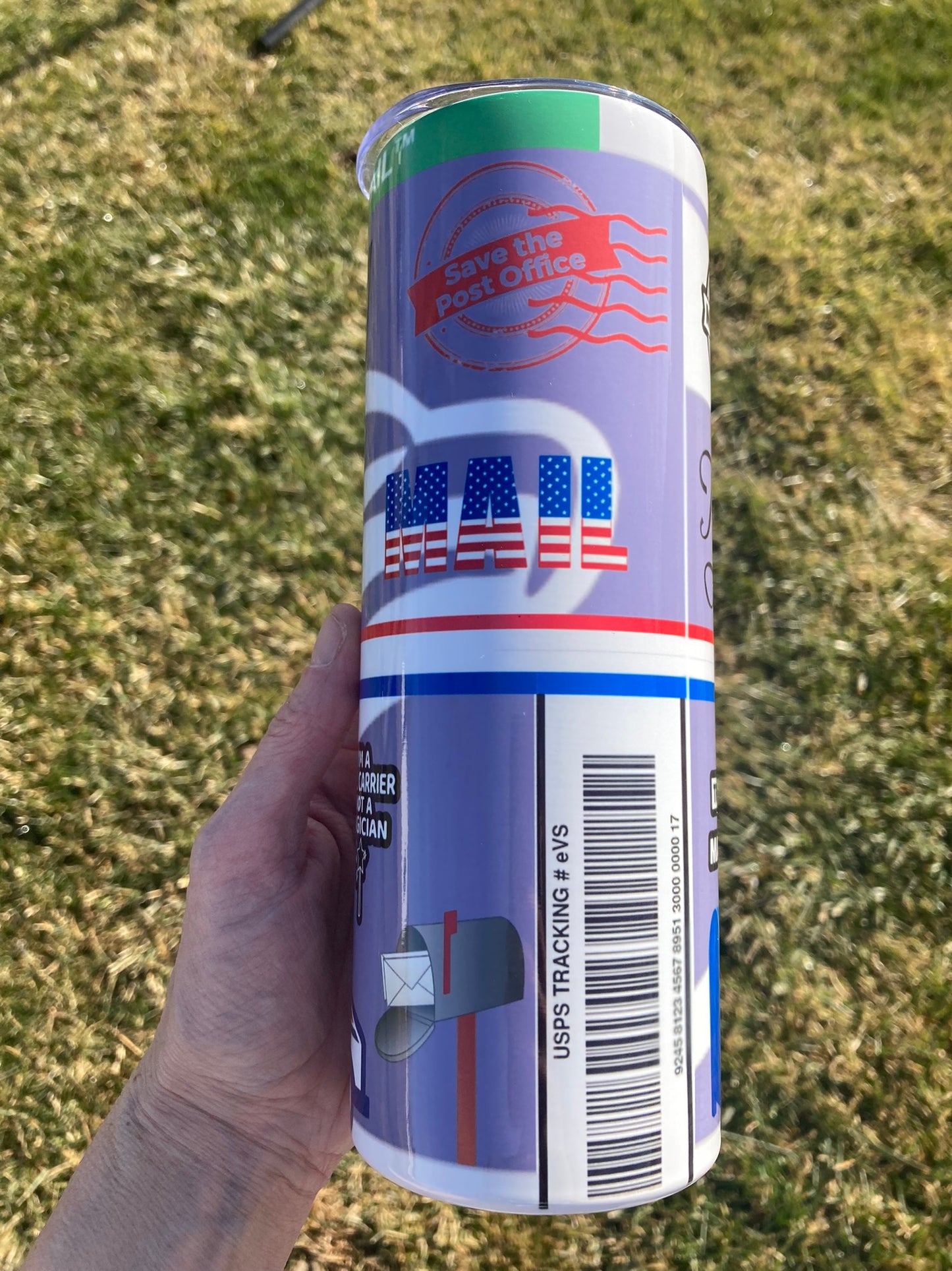 Hand holding a cylindrical can with U.S. Postal Service branding against a grassy background