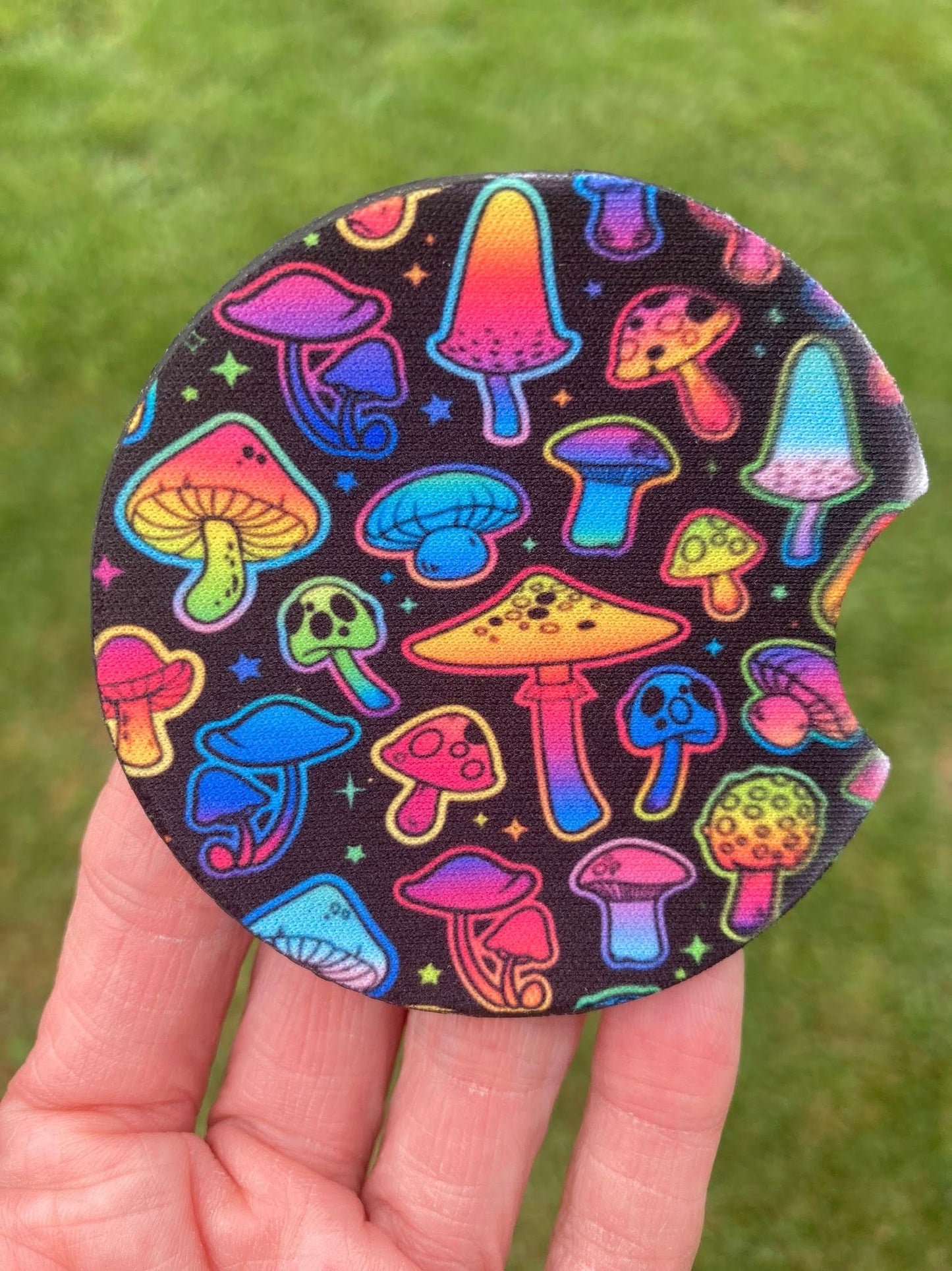 Colorful mushroom patterned coaster held in a hand with grass background