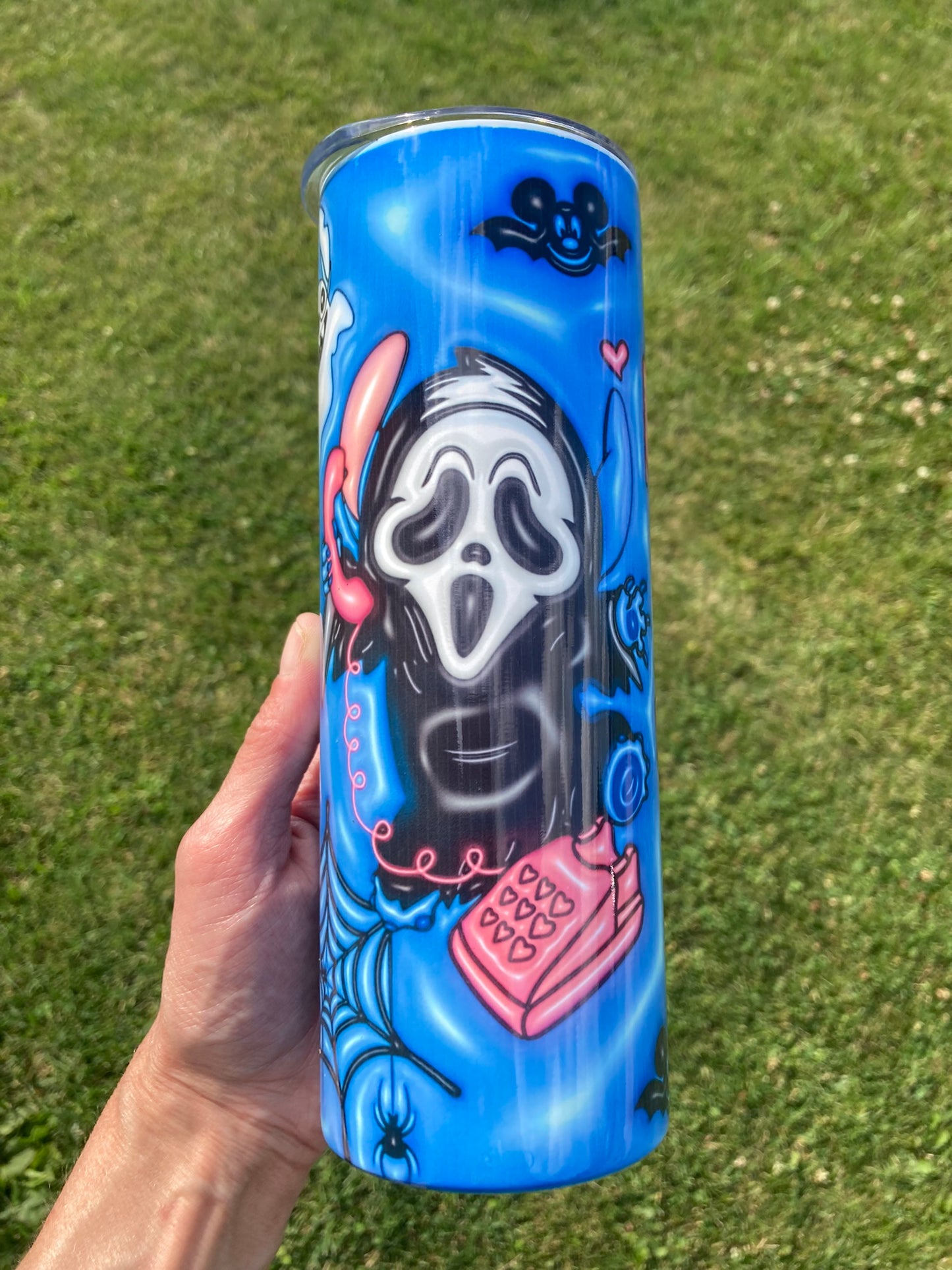 Blue tumbler with a stylized face design held against a grass background