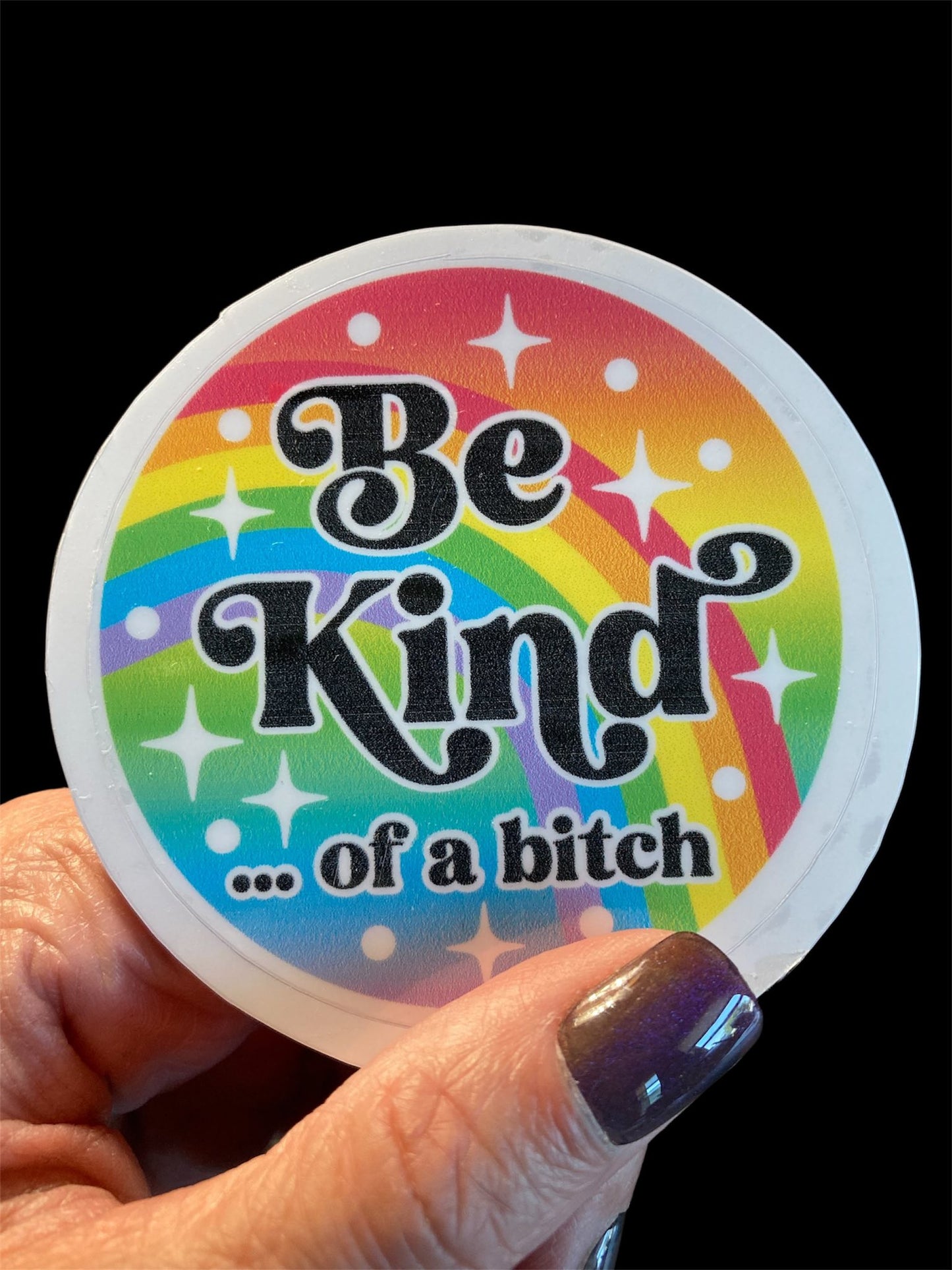 Colorful sticker with 'Be Kind... of a bitch' text held by a hand.