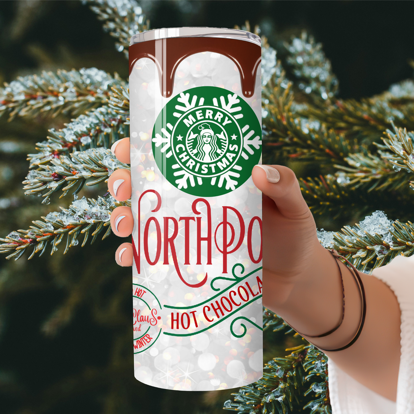 Starbucks tumbler with 'Merry Christmas North Pole Hot Chocolate' design held in front of a Christmas tree.