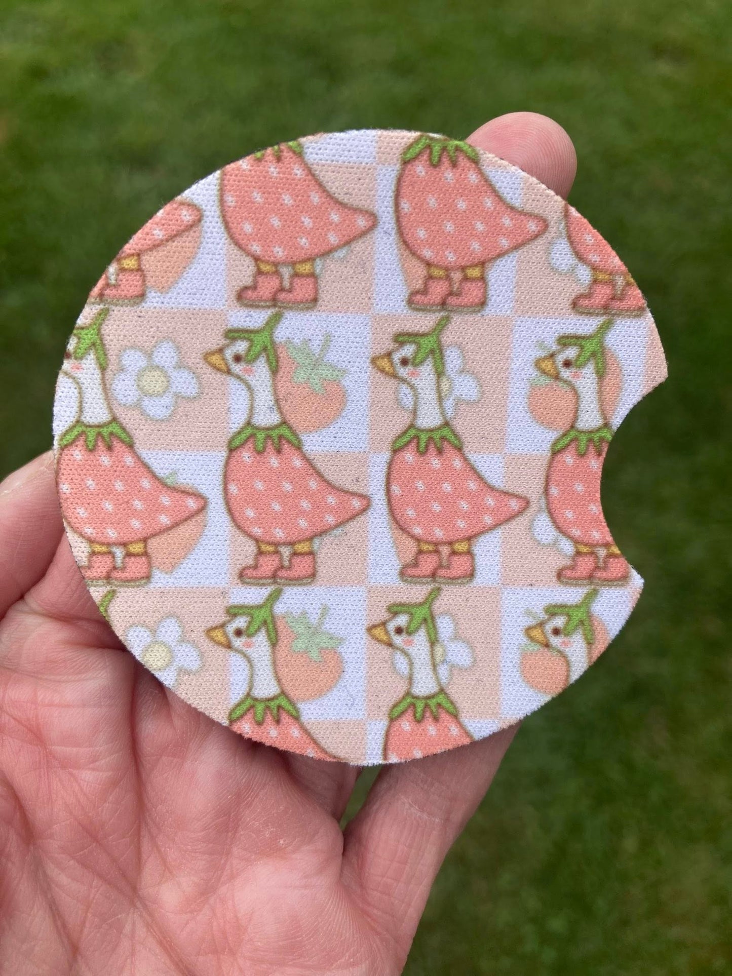 Circular fabric patch with duck pattern held in a hand against a green grass background