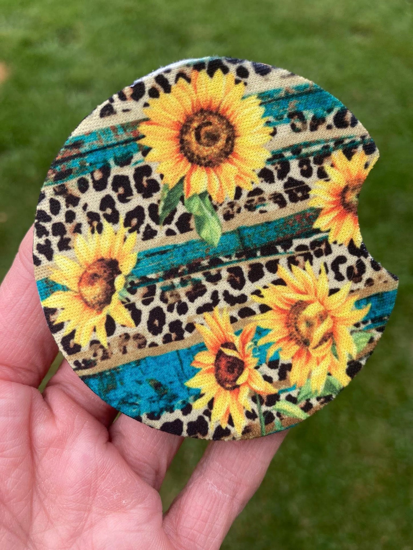 Round coaster with sunflower and leopard print design held in a hand against a green background