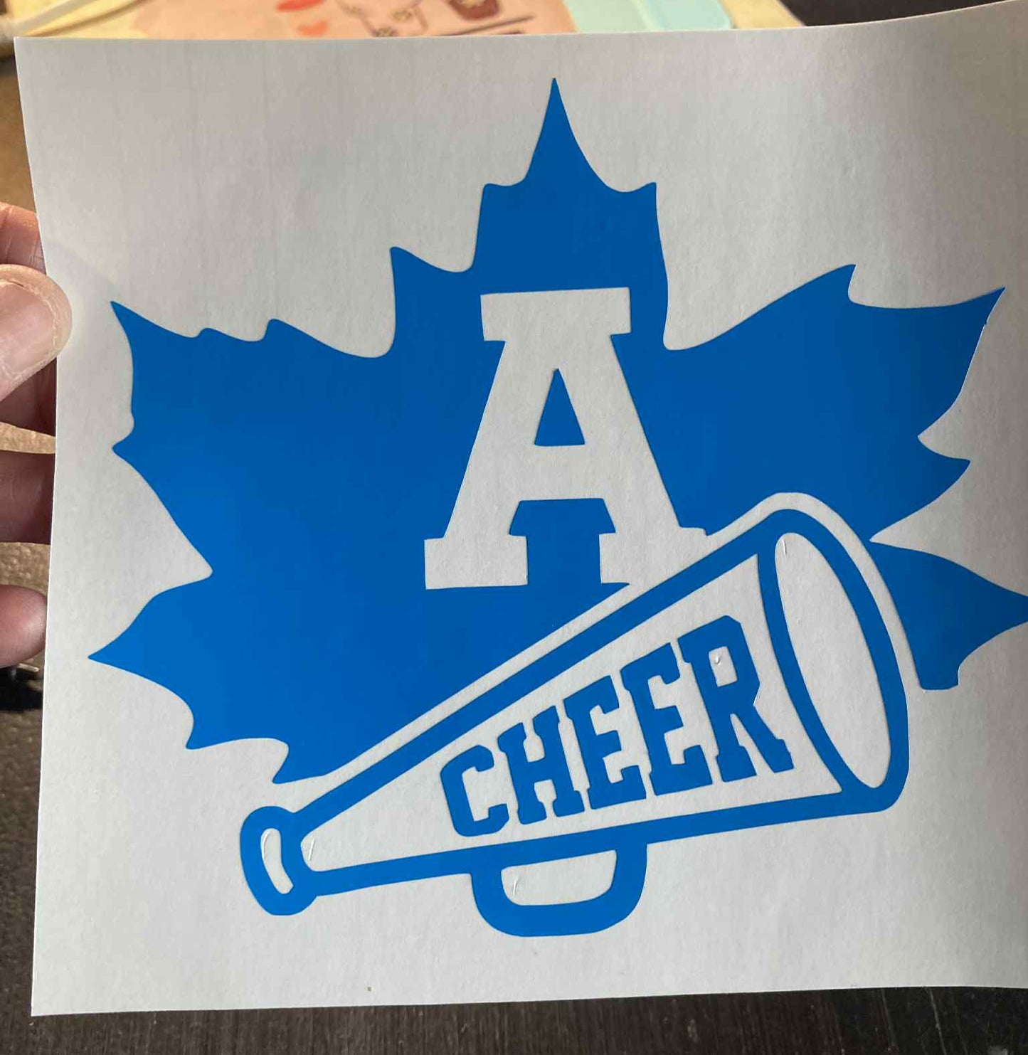 Blue and white 'A Cheer' decal with a maple leaf design on a white background.