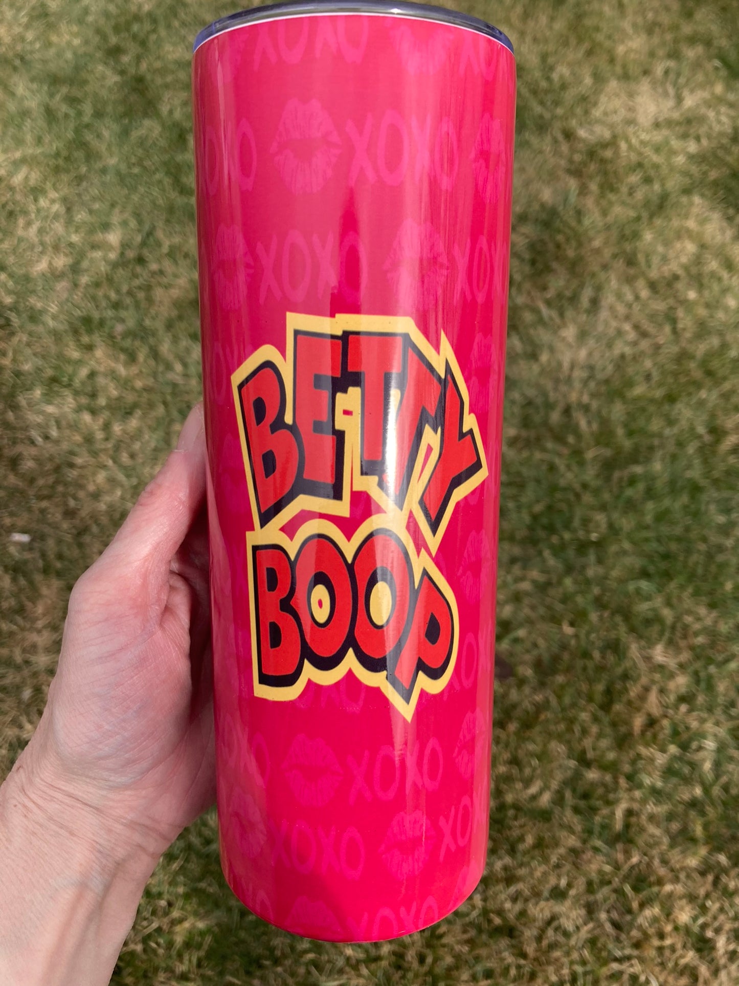 Pink tumbler with 'Betty Boop' branding held by a hand on a grassy background
