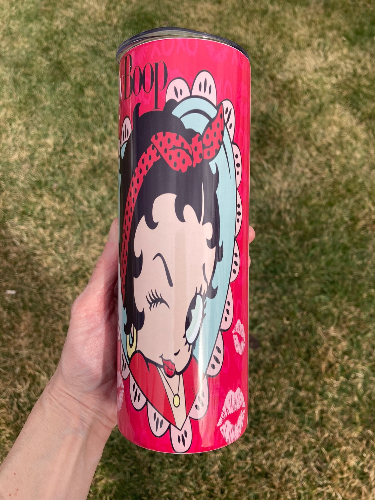 Red cylindrical container with Betty Boop design held by a hand on grass