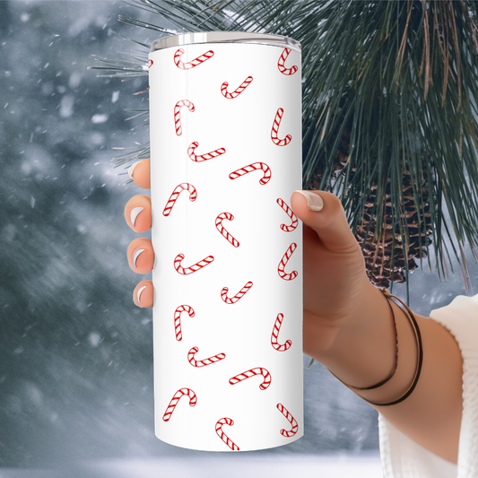 Tumbler with candy cane pattern held by a hand against a snowy background