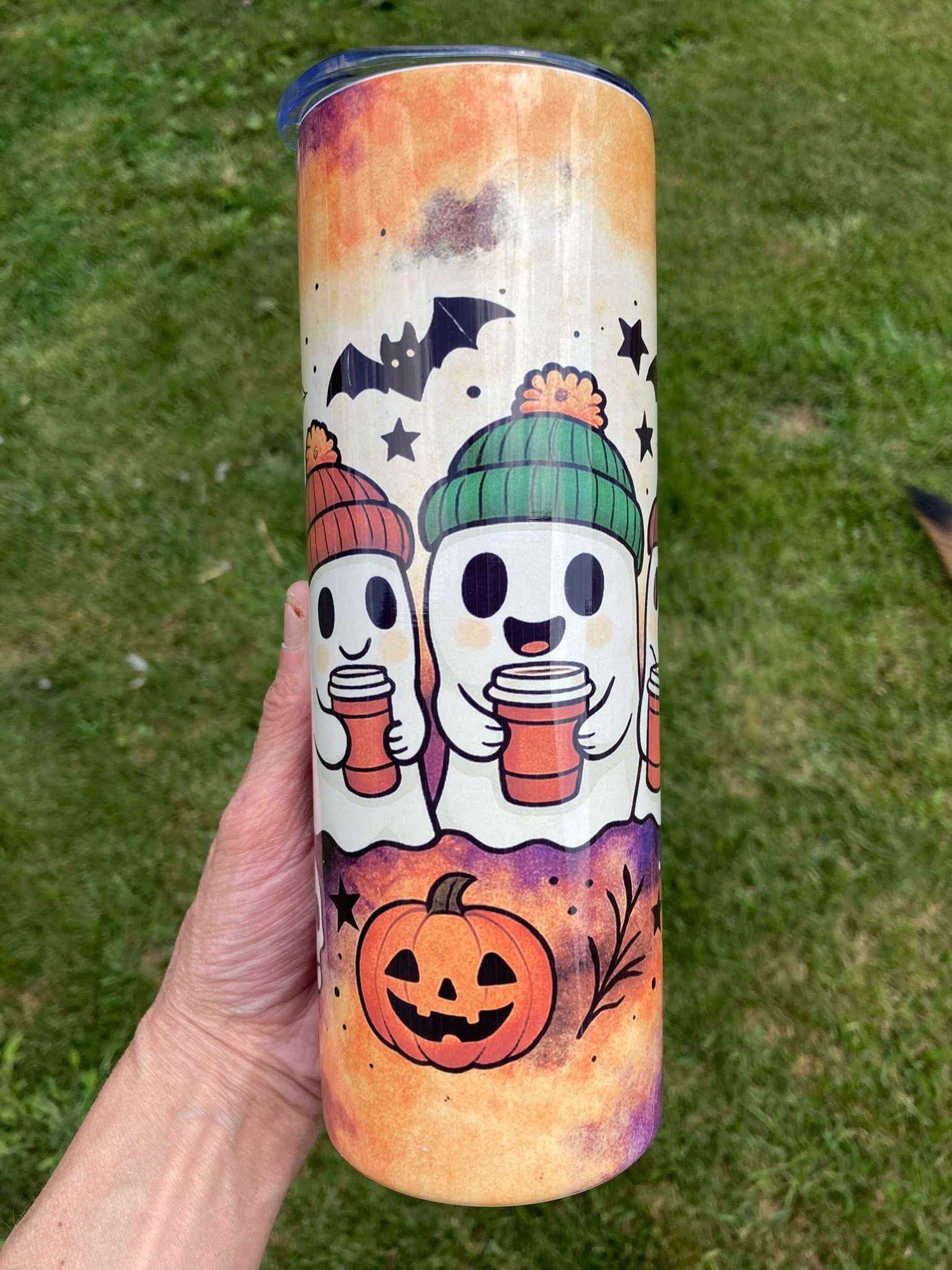 Tumbler with Halloween-themed design featuring ghosts, pumpkins, and bats on a grass background. Cozy ghost tumbler with pumpkins, bats, and ghosts wearing beanies holding coffee cups in fall colors