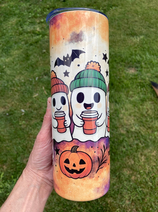 Tumbler with Halloween-themed design featuring ghosts, pumpkins, and bats on a grass background. Cozy ghost tumbler with pumpkins, bats, and ghosts wearing beanies holding coffee cups in fall colors