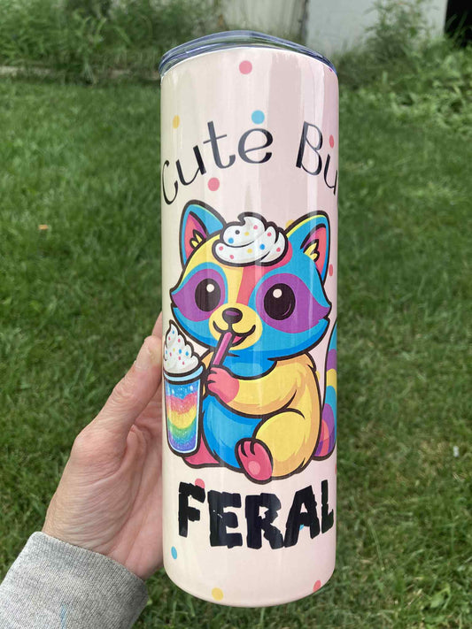 Colorful raccoon tumbler with “Cute But Feral” phrase and rainbow drink design, 20oz insulated skinny stainless steel cup.