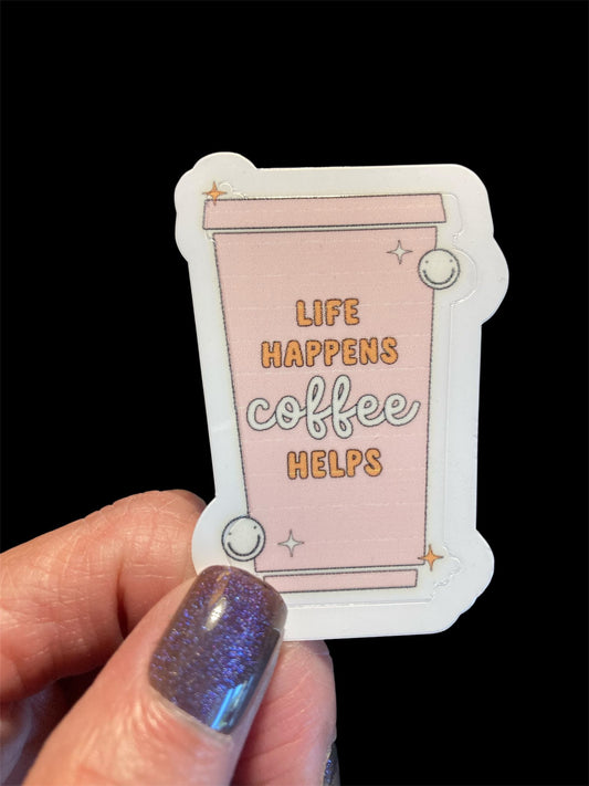 Sticker with 'Life happens, coffee helps' text held by a hand with glittery nail polish.