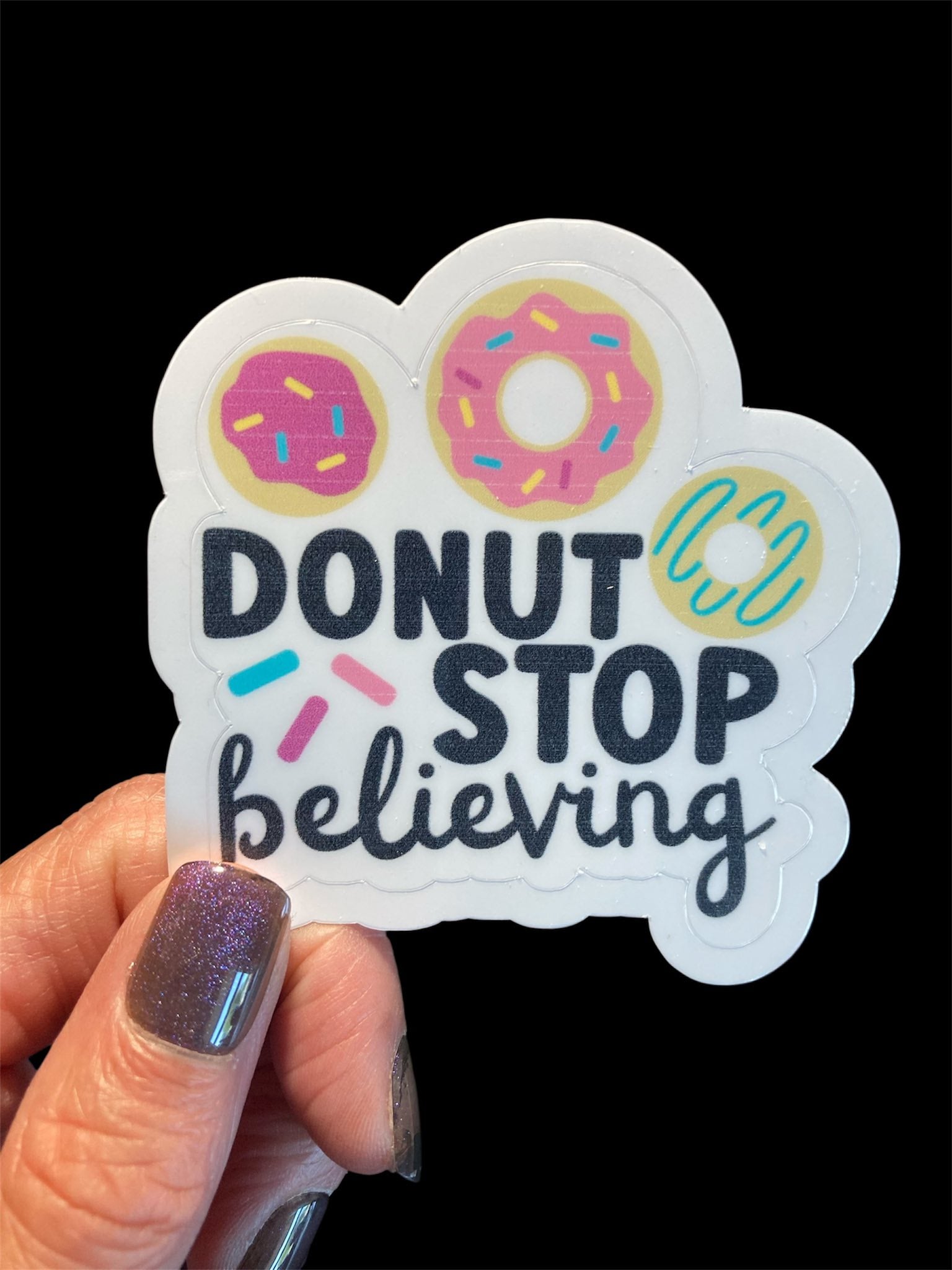 Sticker with 'Donut stop believing' text held by a hand against a black background