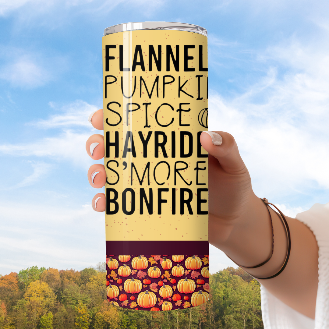Tumbler with autumn-themed text and pumpkin design held against a scenic background. Warm plaid tumbler with “Flannels. Pumpkin Spice. Hayrides. S’mores. Bonfires.” — cozy fall exclusive from MIRootsCreations.