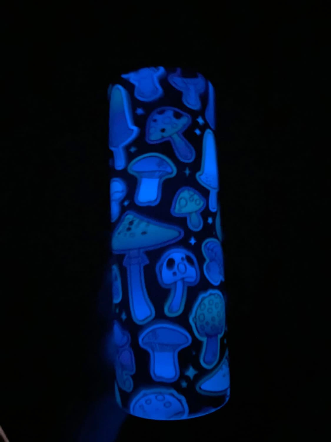 Glowing blue cylindrical container with mushroom patterns on a black background