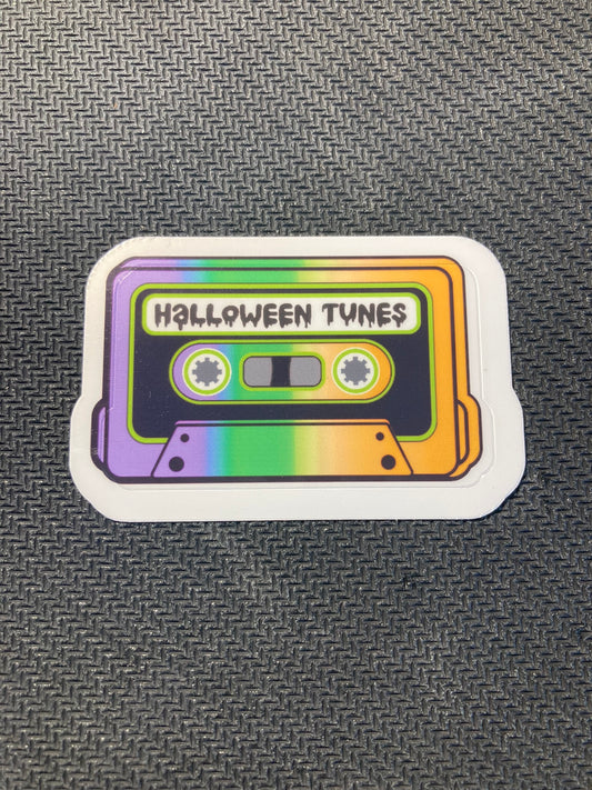 Halloween sticker of a colorful retro cassette tape labeled “Halloween Tunes” in rainbow gradient.
