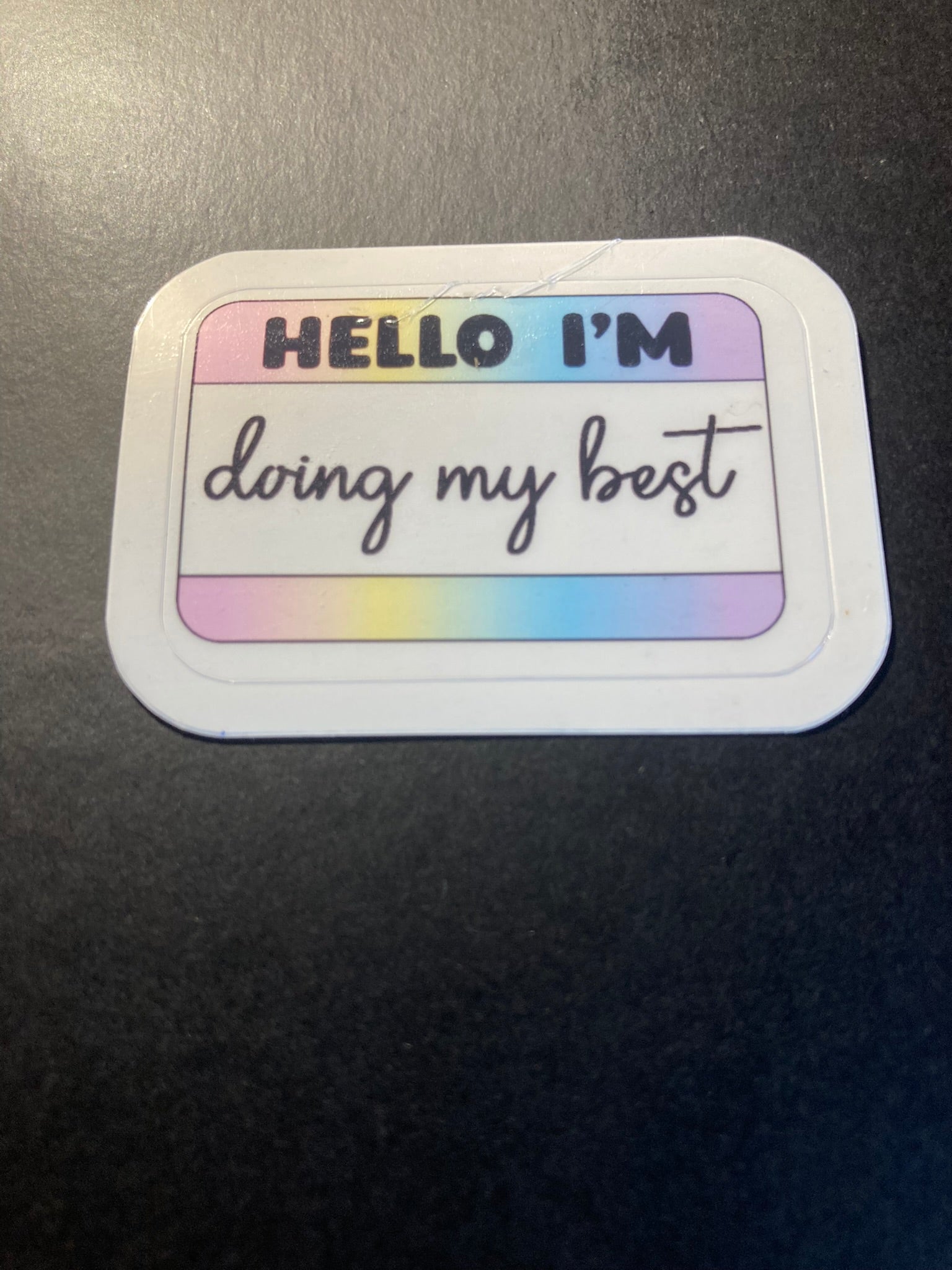 Sticker with 'Hello I'm doing my best' text on a gradient background, attached to a dark surface.