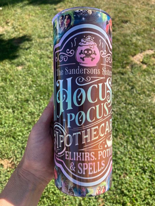 Tumbler with 'Hocus Pocus' design held in a hand against a grassy background. Hocus Pocus apothecary tumbler with potion bottle design and colorful witch themed background