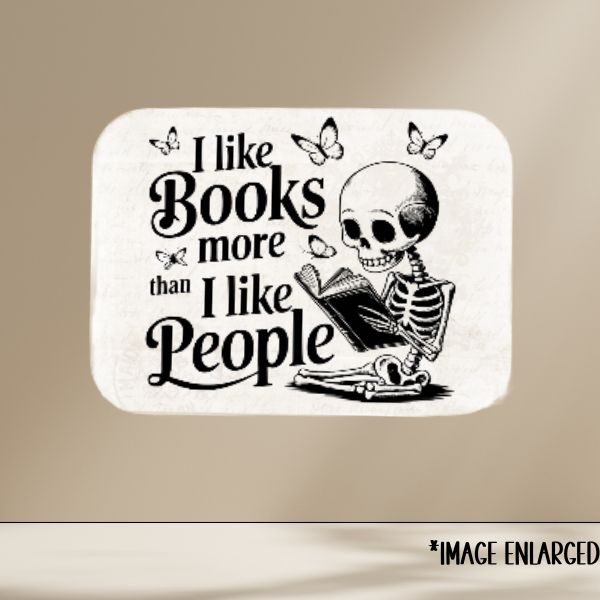 Skeletal figure reading a book with text 'I like books more than I like people' on a beige background.
