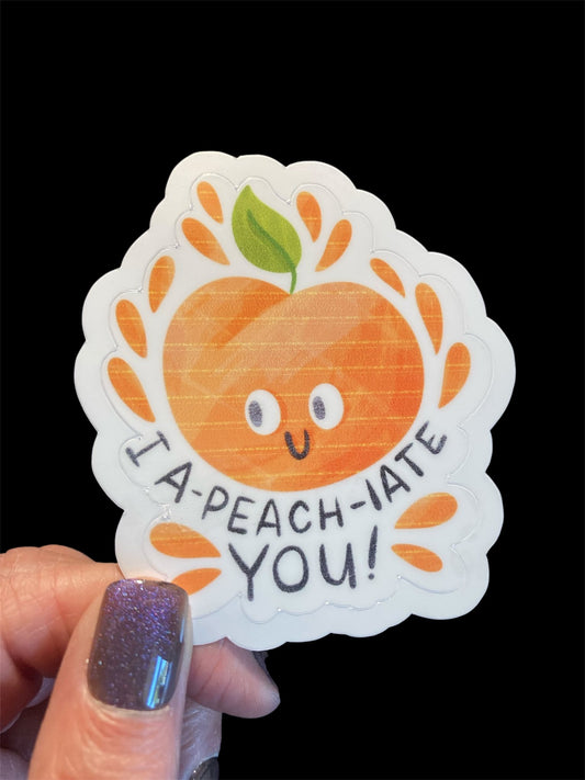 Sticker with a peach design and text held by a hand against a black background