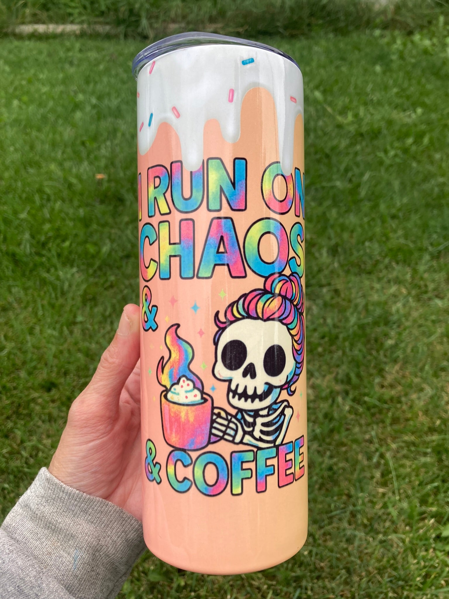 Tumbler with colorful design and text held in a hand against a grass background