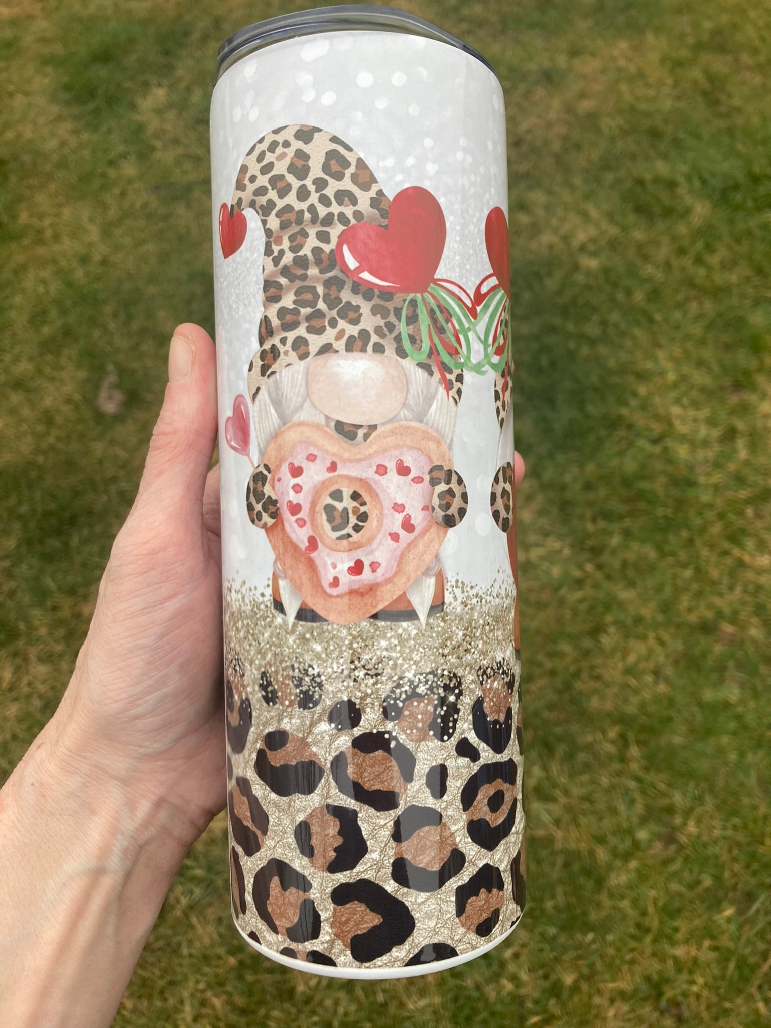 Tumbler with decorative design held by a hand on a grassy background