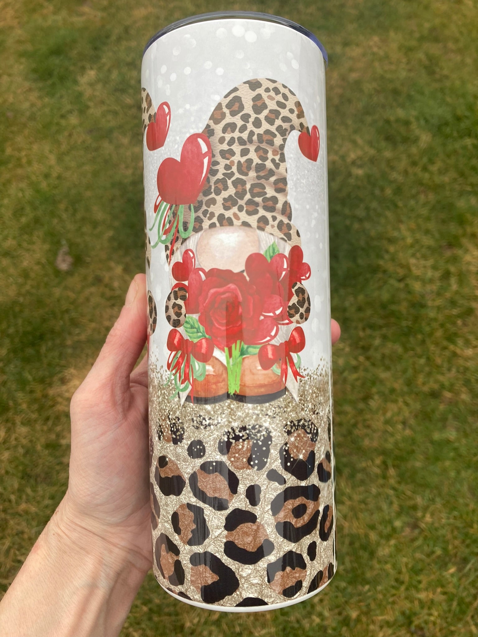Tumbler with artistic design of a character holding flowers, held by a hand against a grassy background.