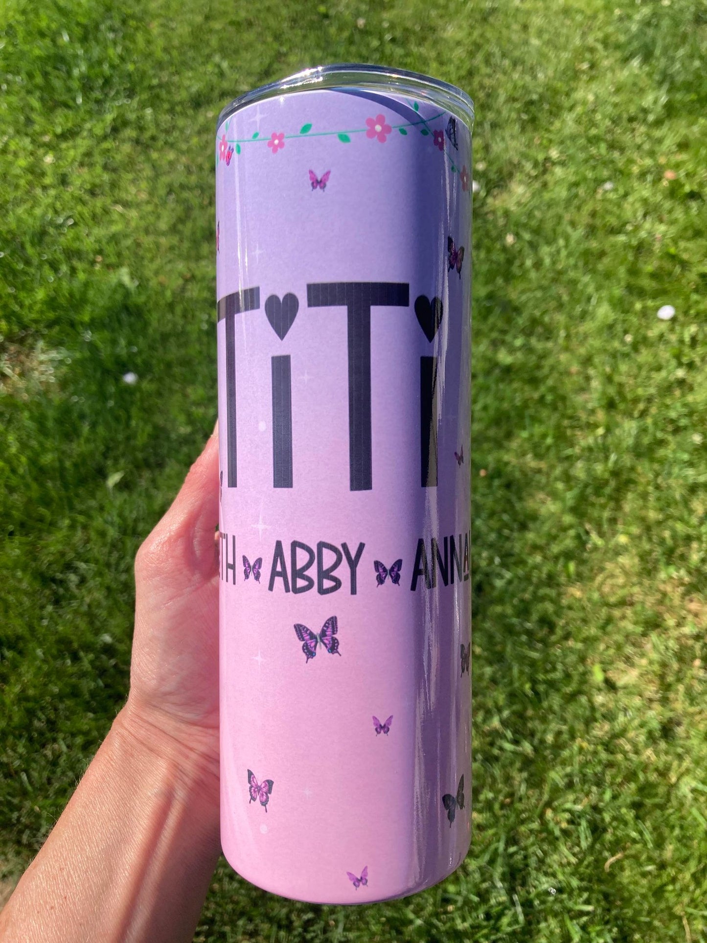 Purple tumbler with text held in a hand on grass