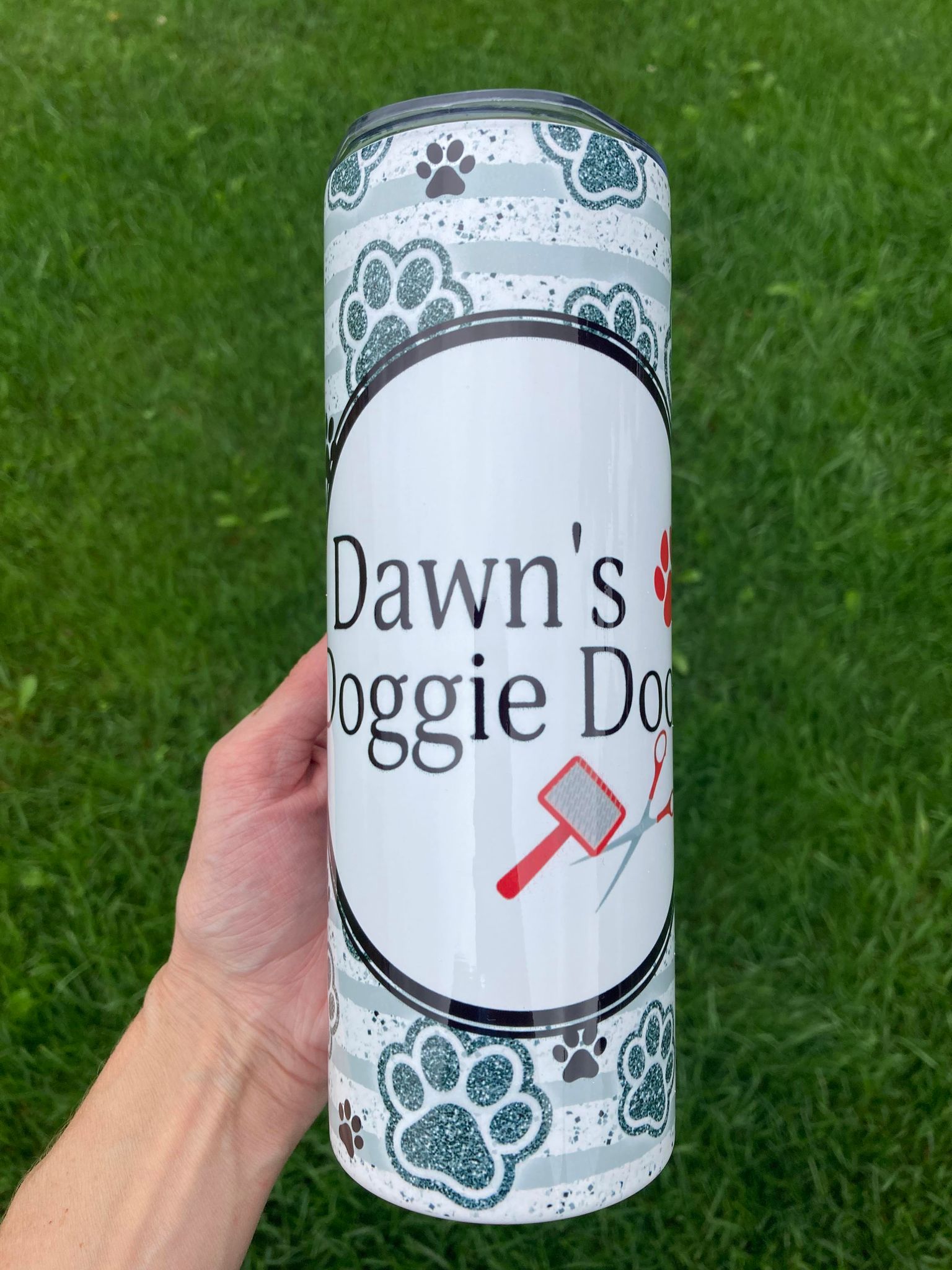 Tumbler with 'Dawn's Doggie Day' design held in front of grass