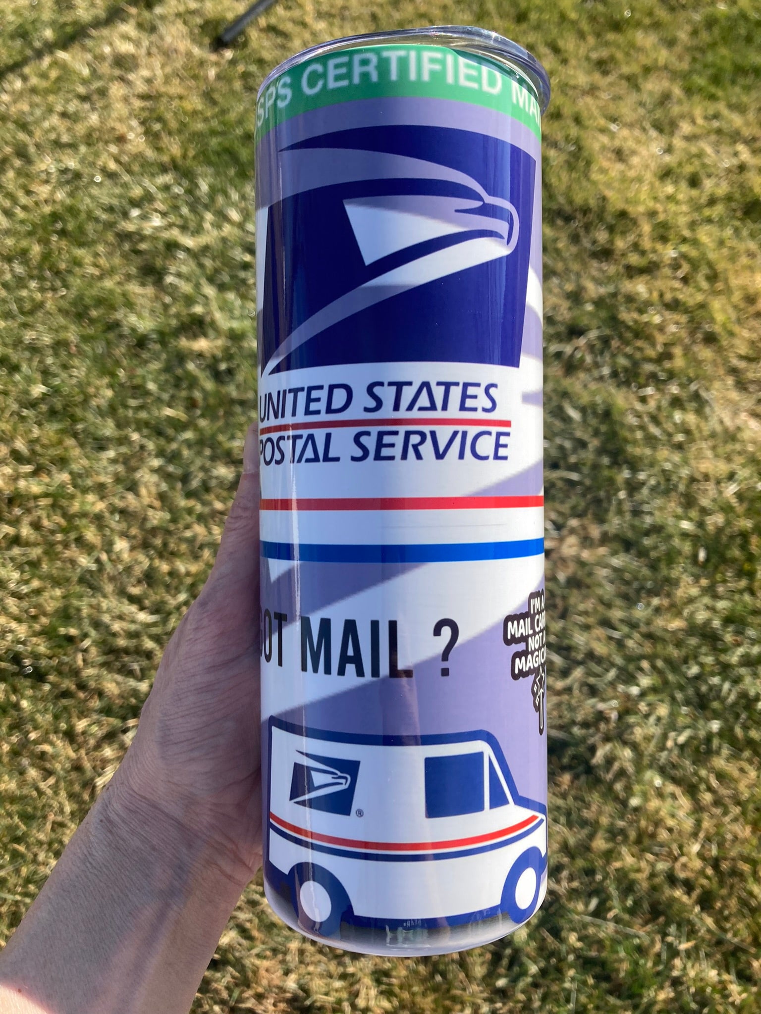 Canister with United States Postal Service branding held in a hand against a grassy background