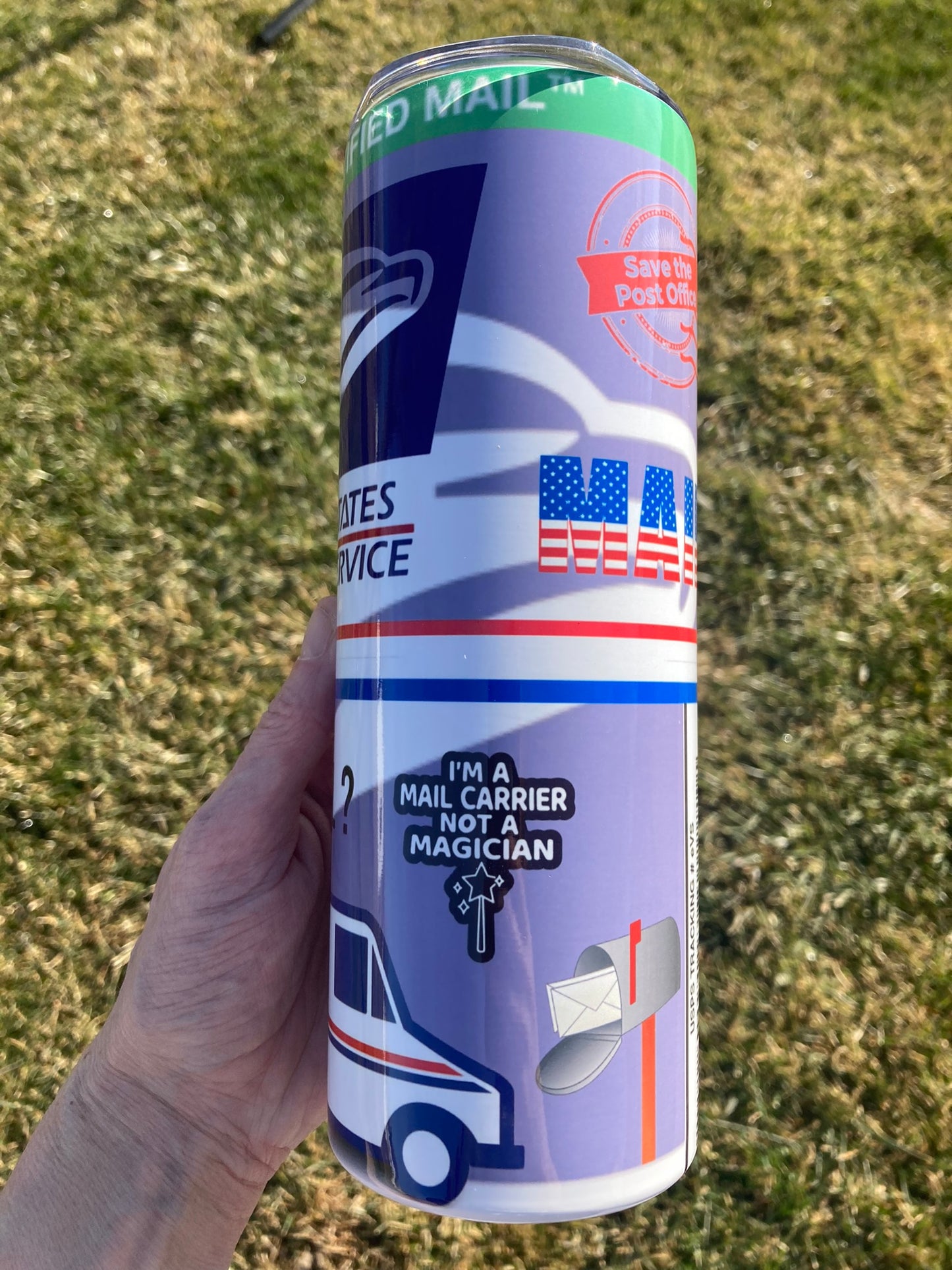 Hand holding a can with postal service-themed design on a grassy background