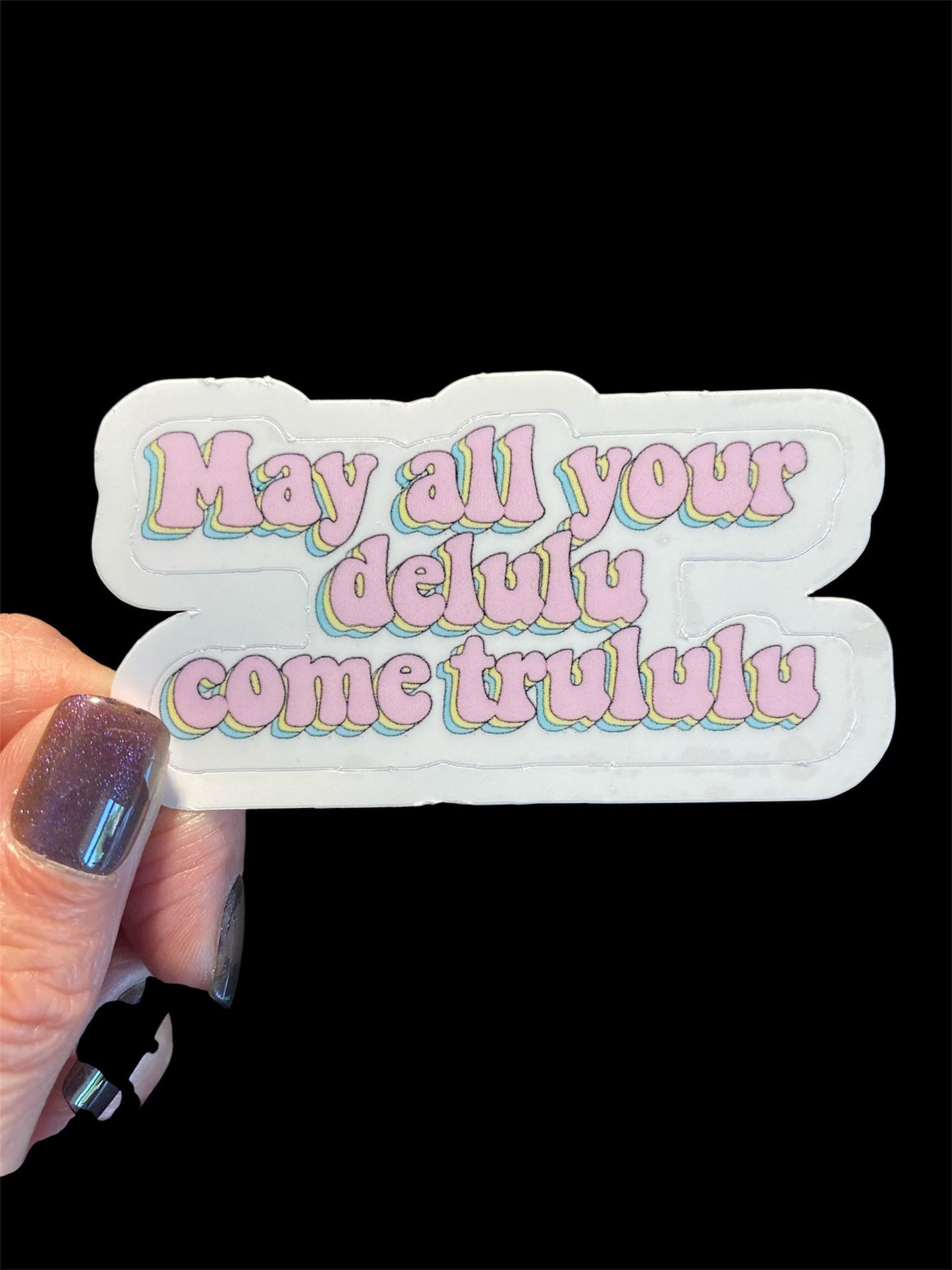 Sticker with colorful text held by a hand against a black background