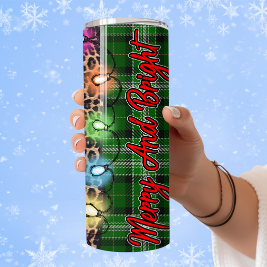 Tumbler with 'Merry And Bright' text and Christmas lights design held by a hand against a snowy background.