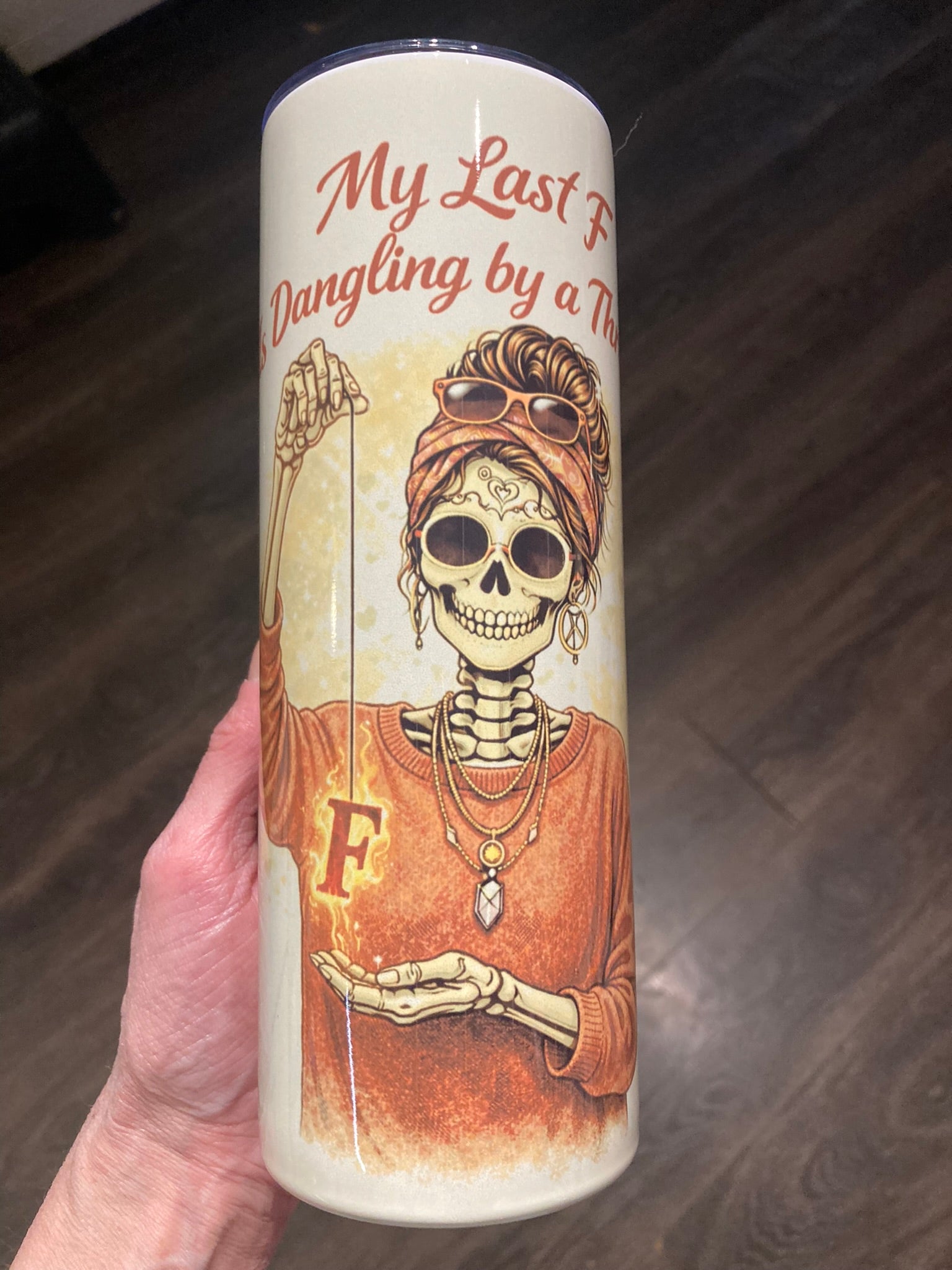 Skeleton woman holding a flaming letter F dangling by a string with “My Last F Is Dangling by a Thread” text on a tumbler.