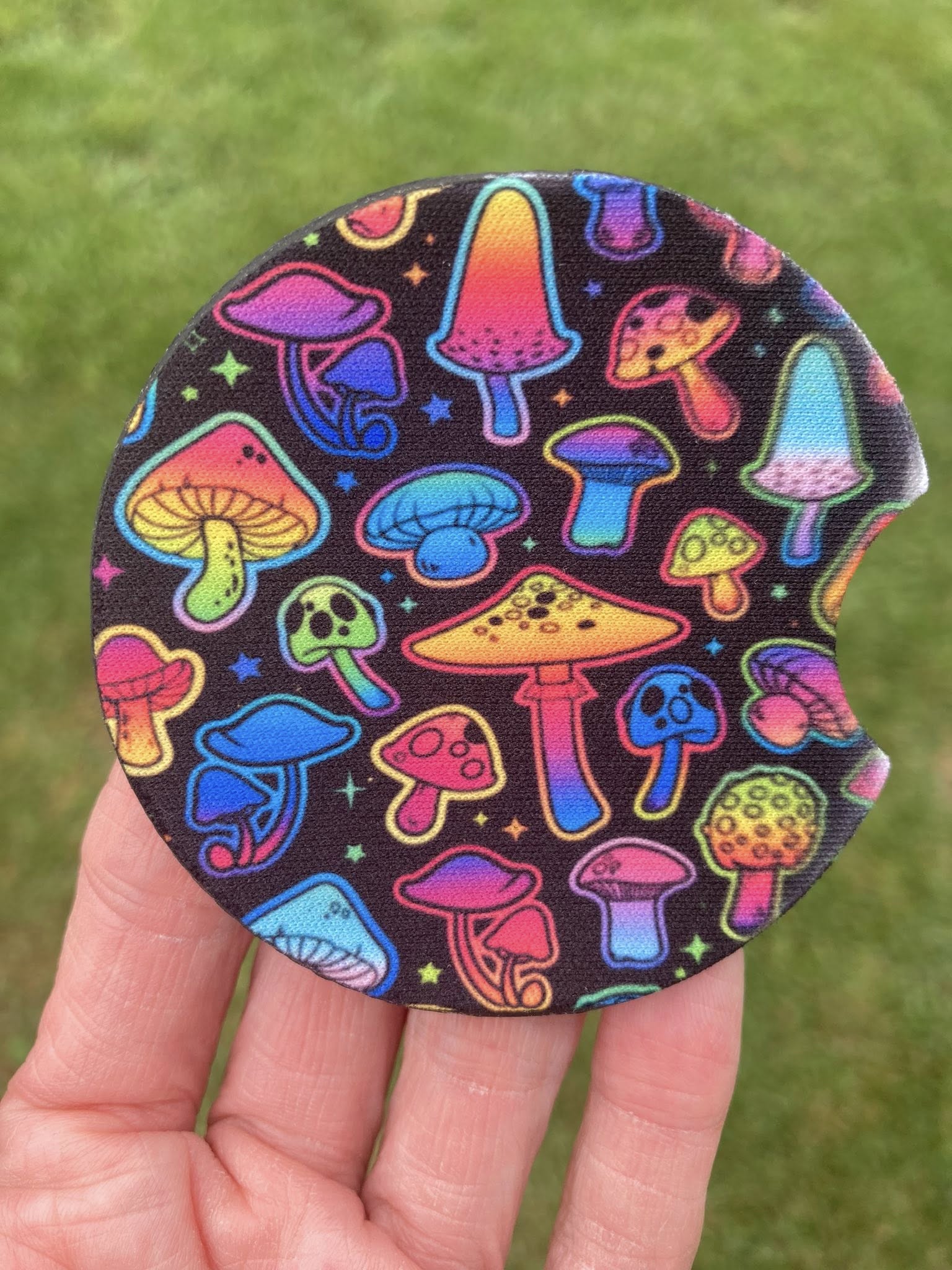Colorful mushroom patterned coaster held in a hand with grass background