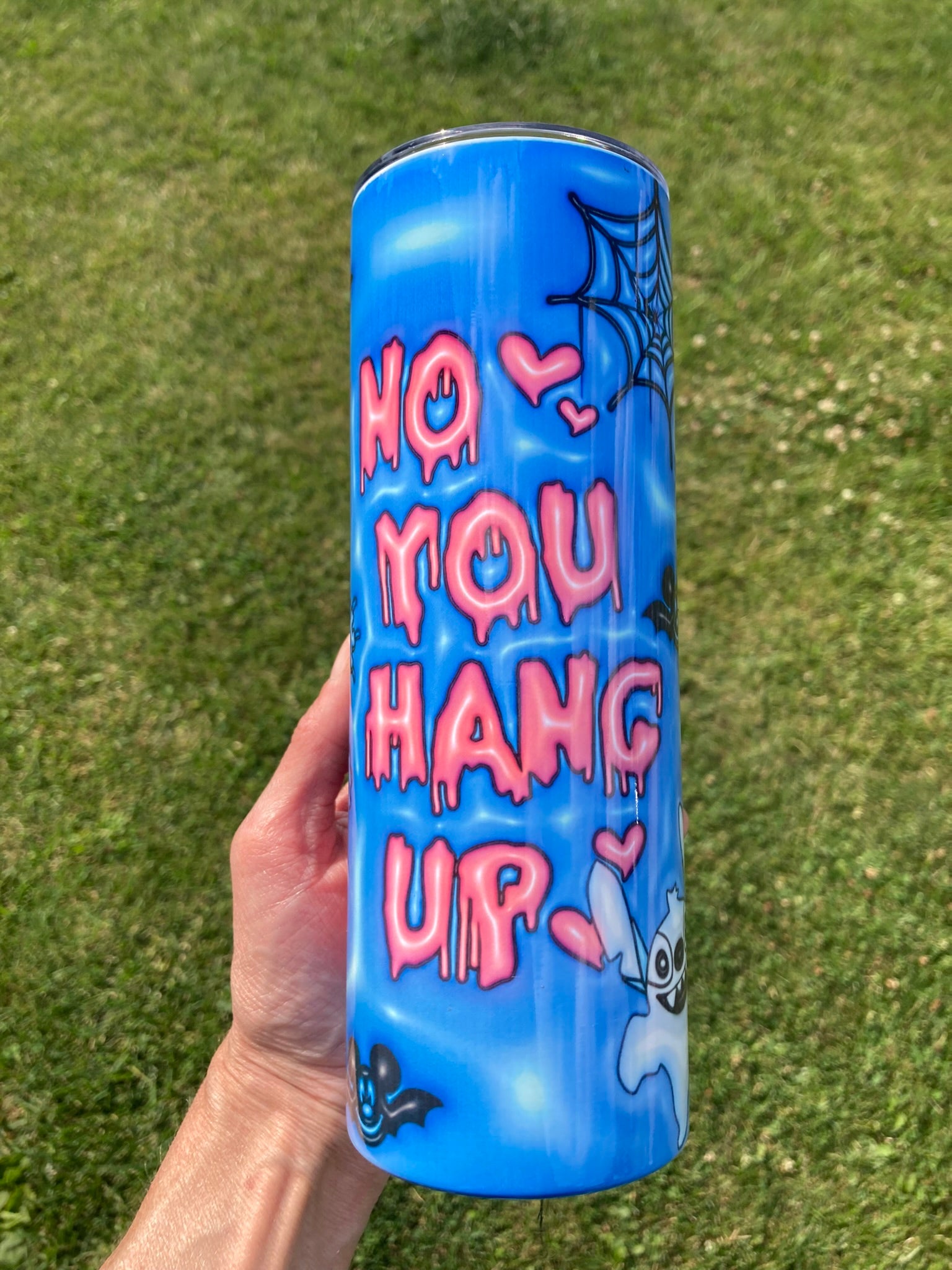 Blue tumbler with pink text held in a hand against a grass background