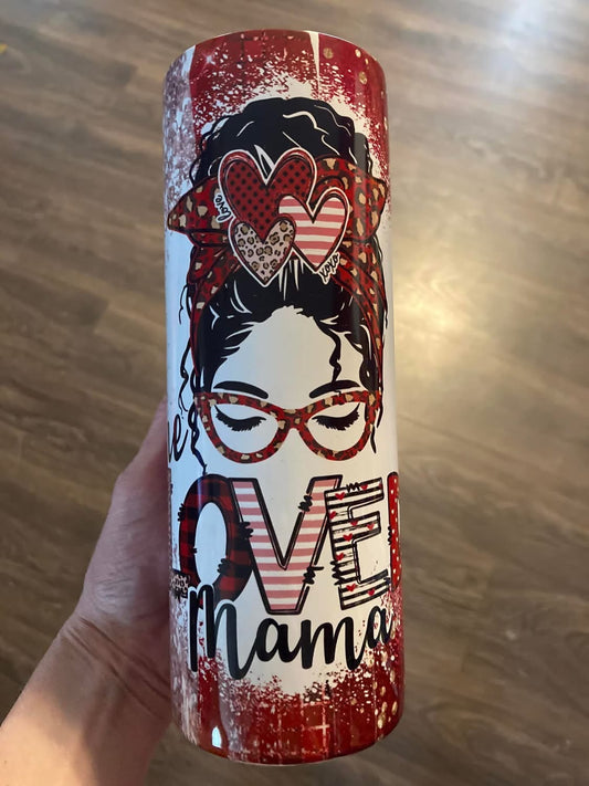 Tumbler with decorative design and text held by a hand on a wooden surface. 20oz skinny tumbler featuring messy bun mama design with red plaid, leopard print, and heart sunglasses with “One Loved Mama” text