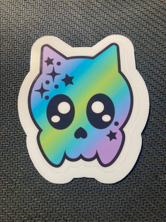 Halloween sticker with pastel rainbow cat skull design decorated with sparkles and stars.