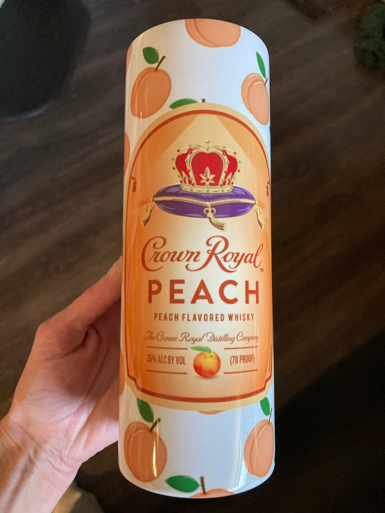 Crown Royal Peach whisky can held by a hand on a wooden surface