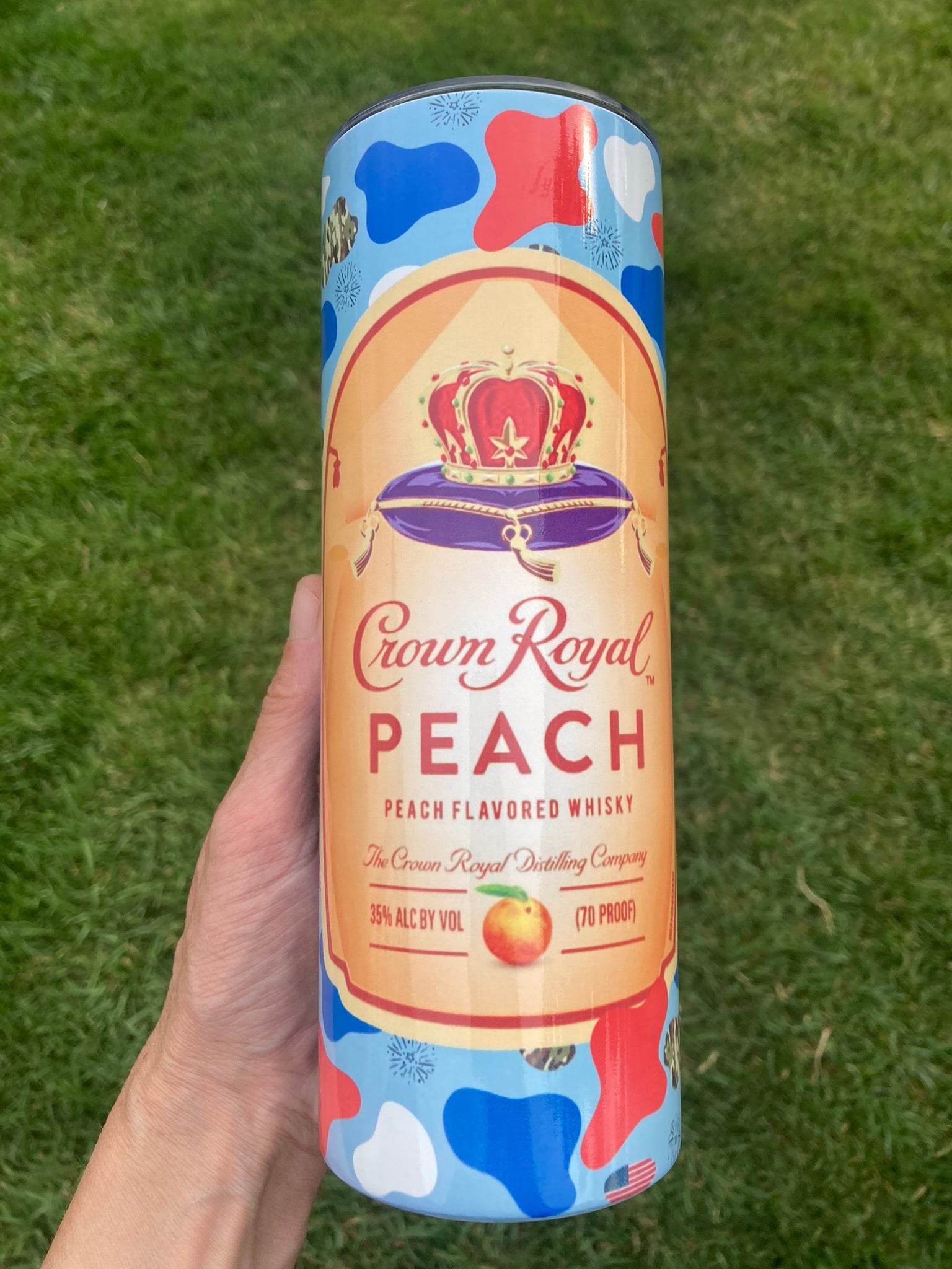 Crown Royal Peach whisky can held in a hand against a grassy background