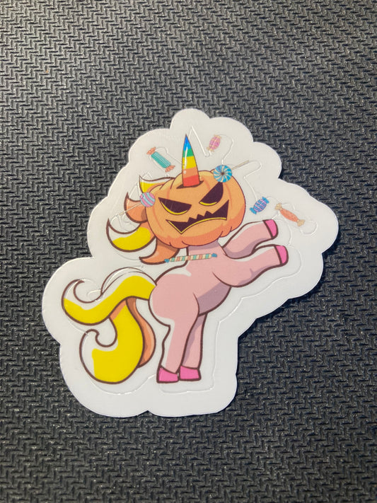Halloween sticker of a unicorn with a jack-o’-lantern pumpkin head, rainbow horn, and candy accents.