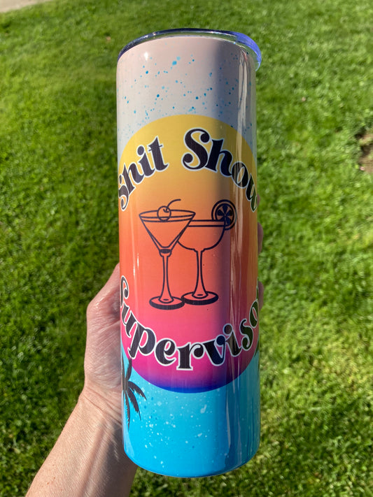 Tumbler with colorful design and text held against a grass background