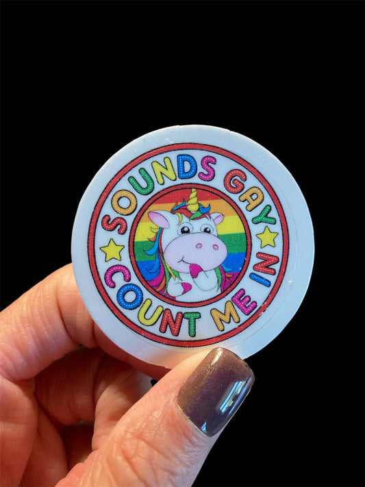 Sticker with unicorn and rainbow design held by a hand against a black background