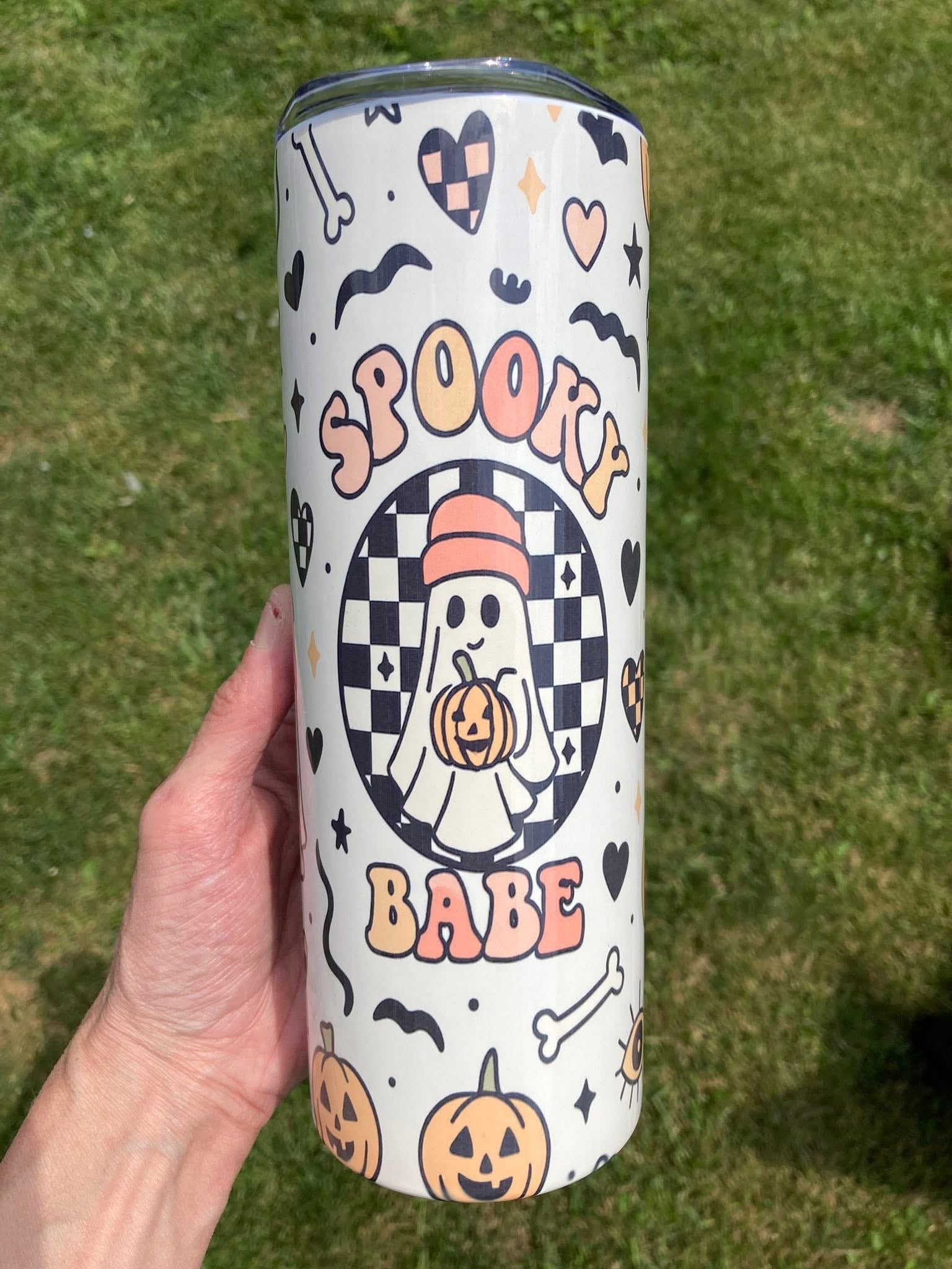 Spooky babe tumbler with cute ghost holding pumpkin surrounded by hearts, bats, and checkerboard pattern