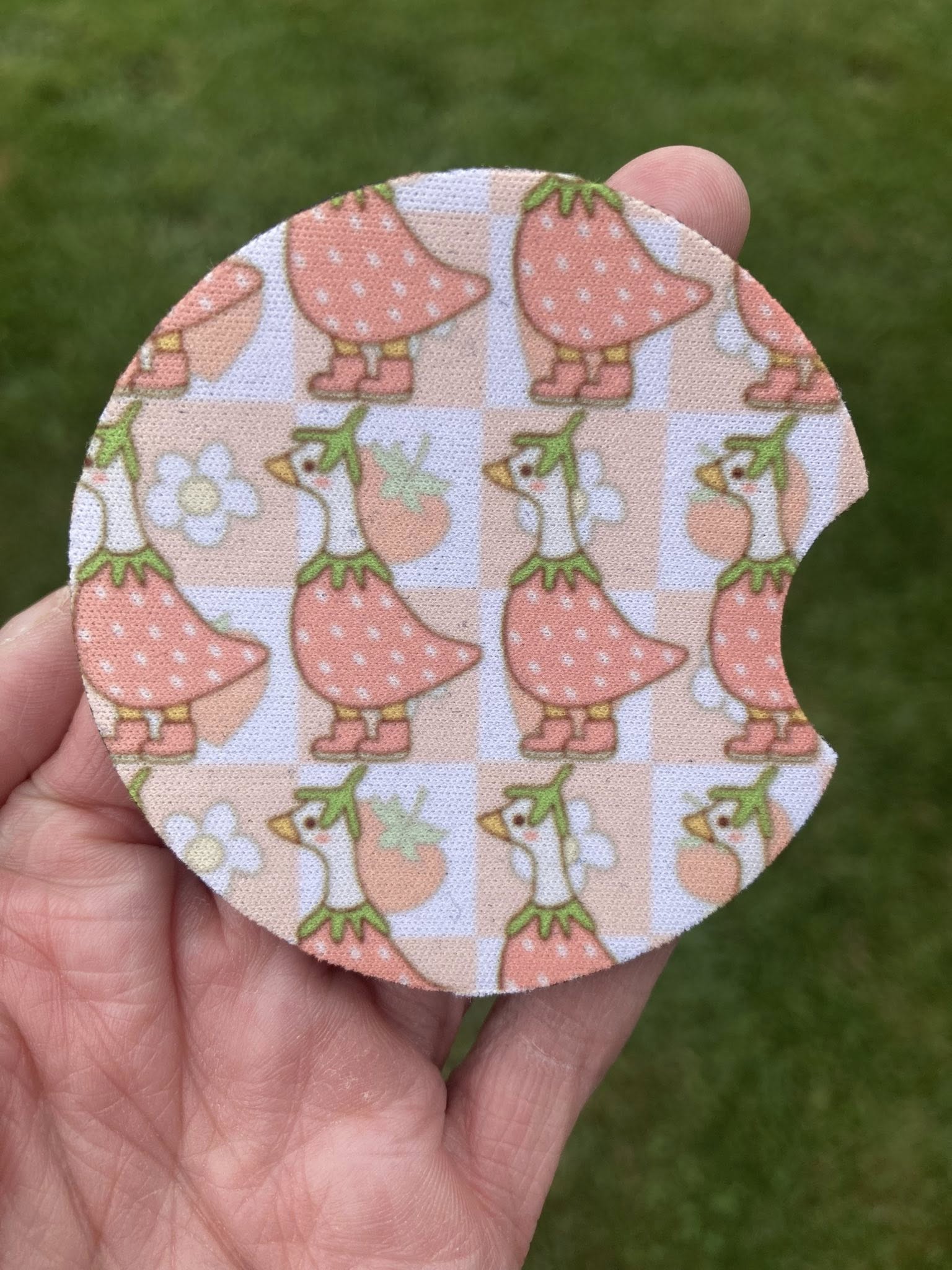 Circular fabric patch with duck pattern held in a hand against a green grass background